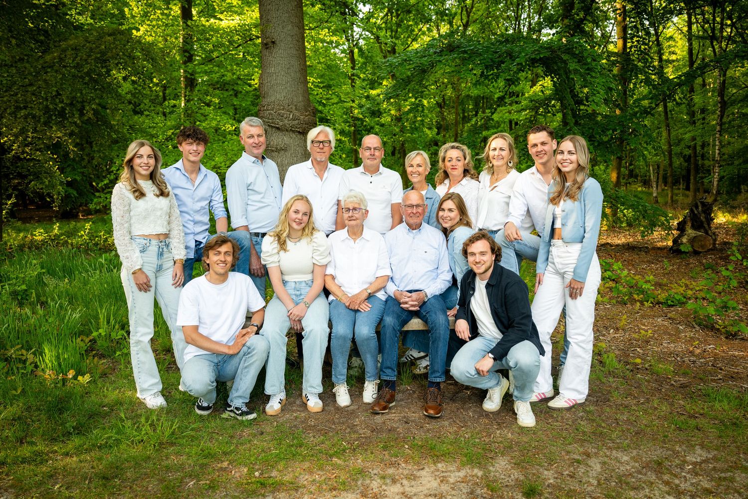 Large family group wearing white and denim poses together in outdoor woodland setting.