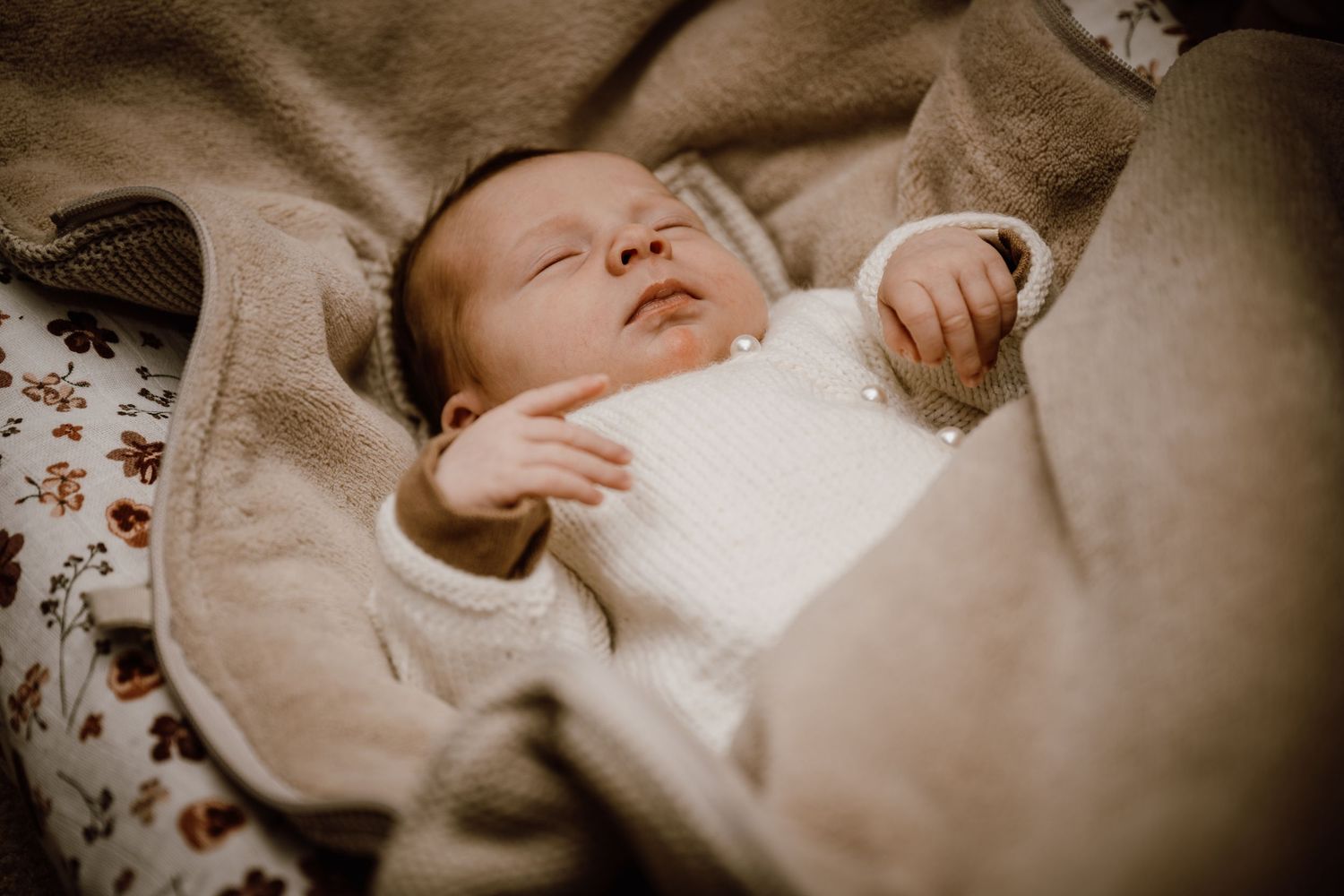 A baby sleeps peacefully in soft white bedding surrounded by delicate floral patterns.