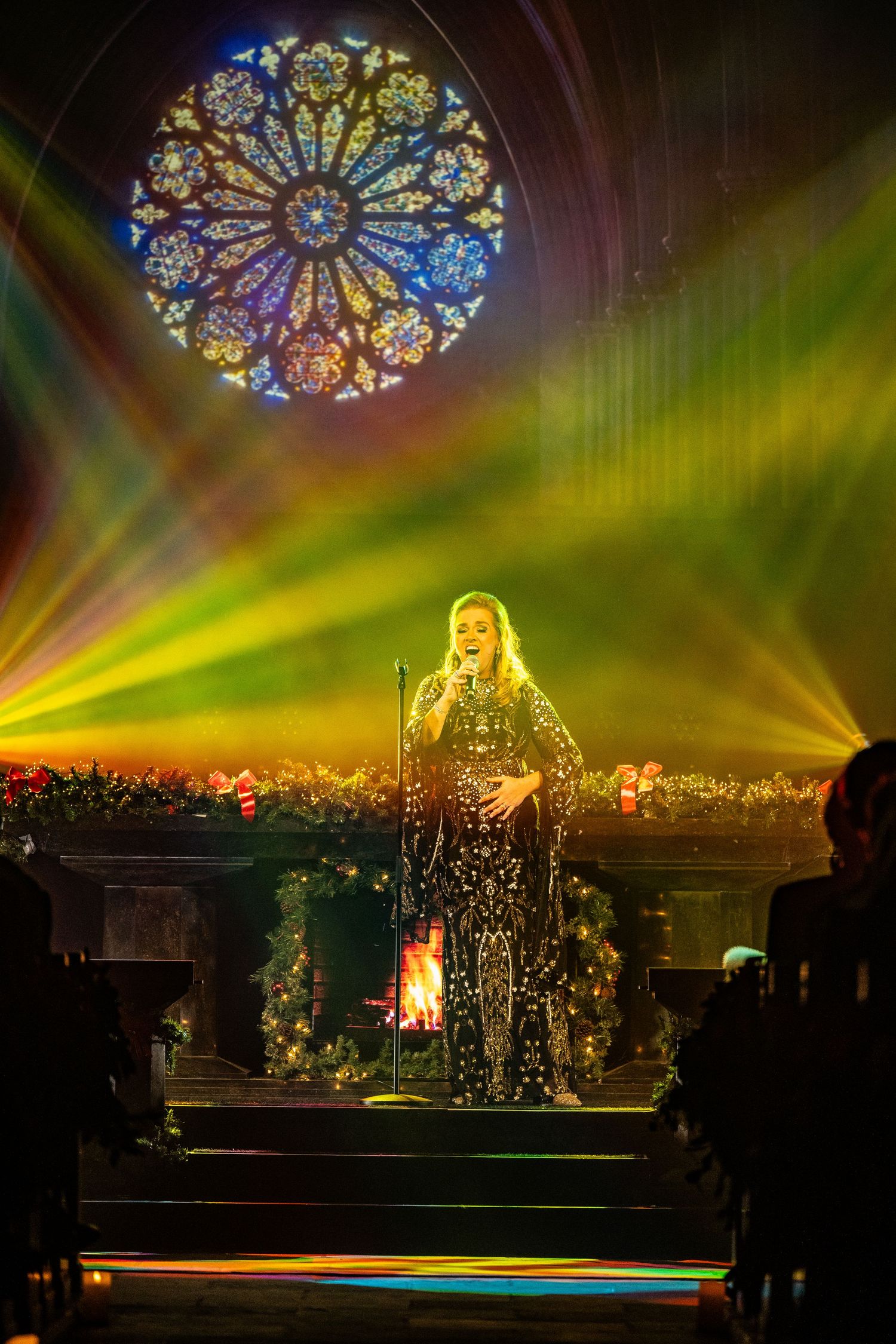 Concert performance under ornate stained glass windows with dramatic green and gold lighting effects.