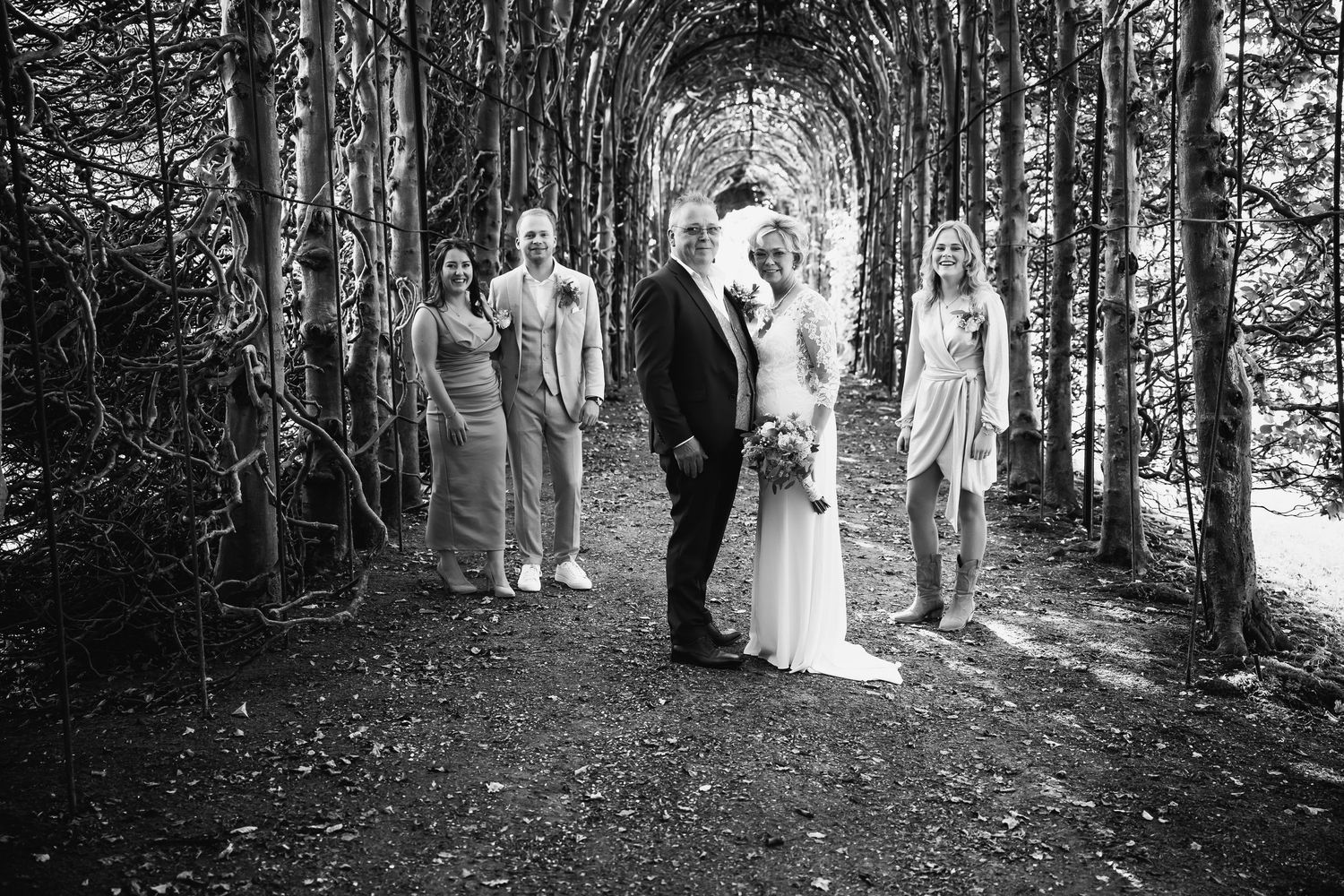 Wedding party walking through a wooded forest path on a sunny afternoon.