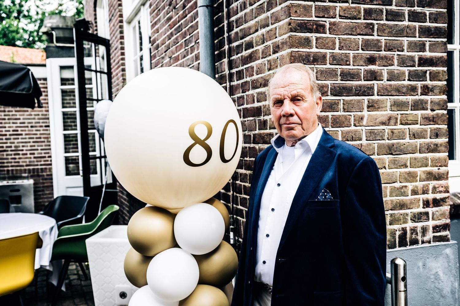 Festive outdoor celebration with white and gold balloons against a brick building facade.