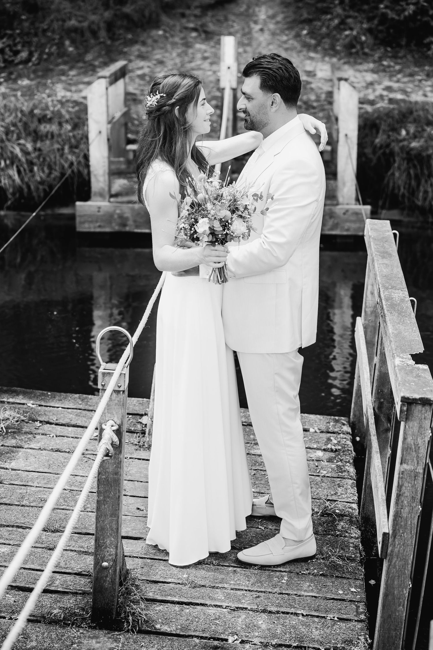 Black and white wedding photos captured on a rustic wooden dock by the water.