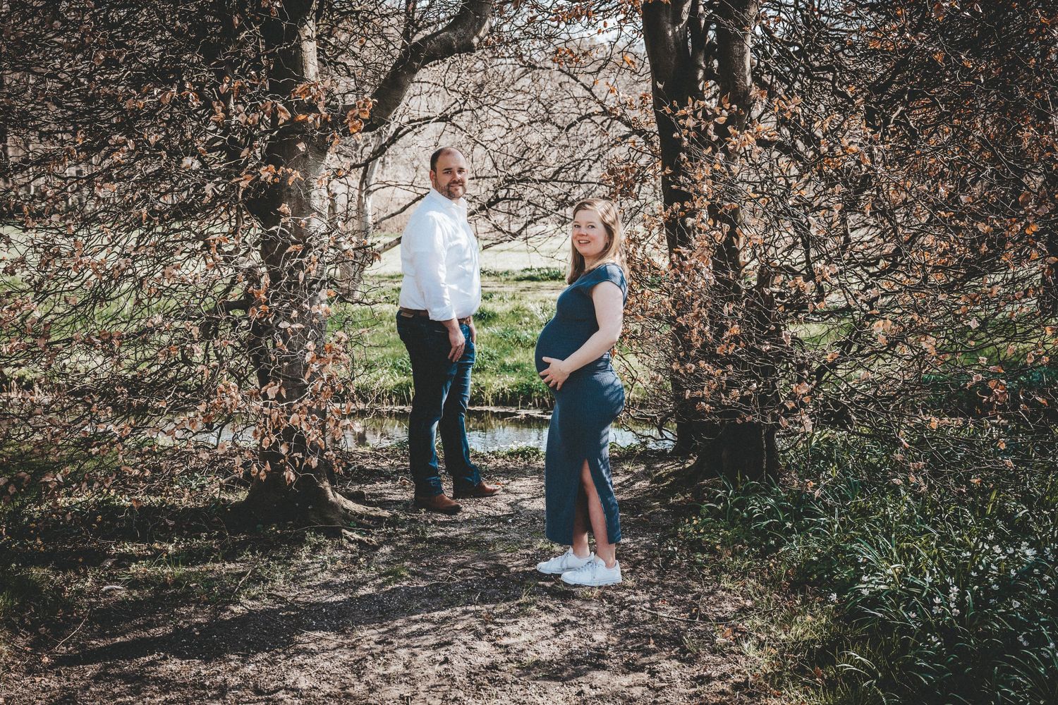 Outdoor maternity photography session among autumn trees and natural scenery.