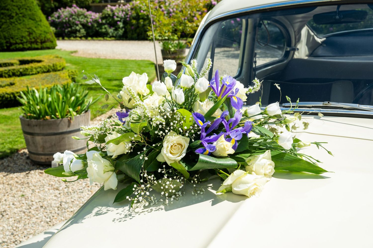 White and purple floral wedding car decorations arranged on a vehicle.