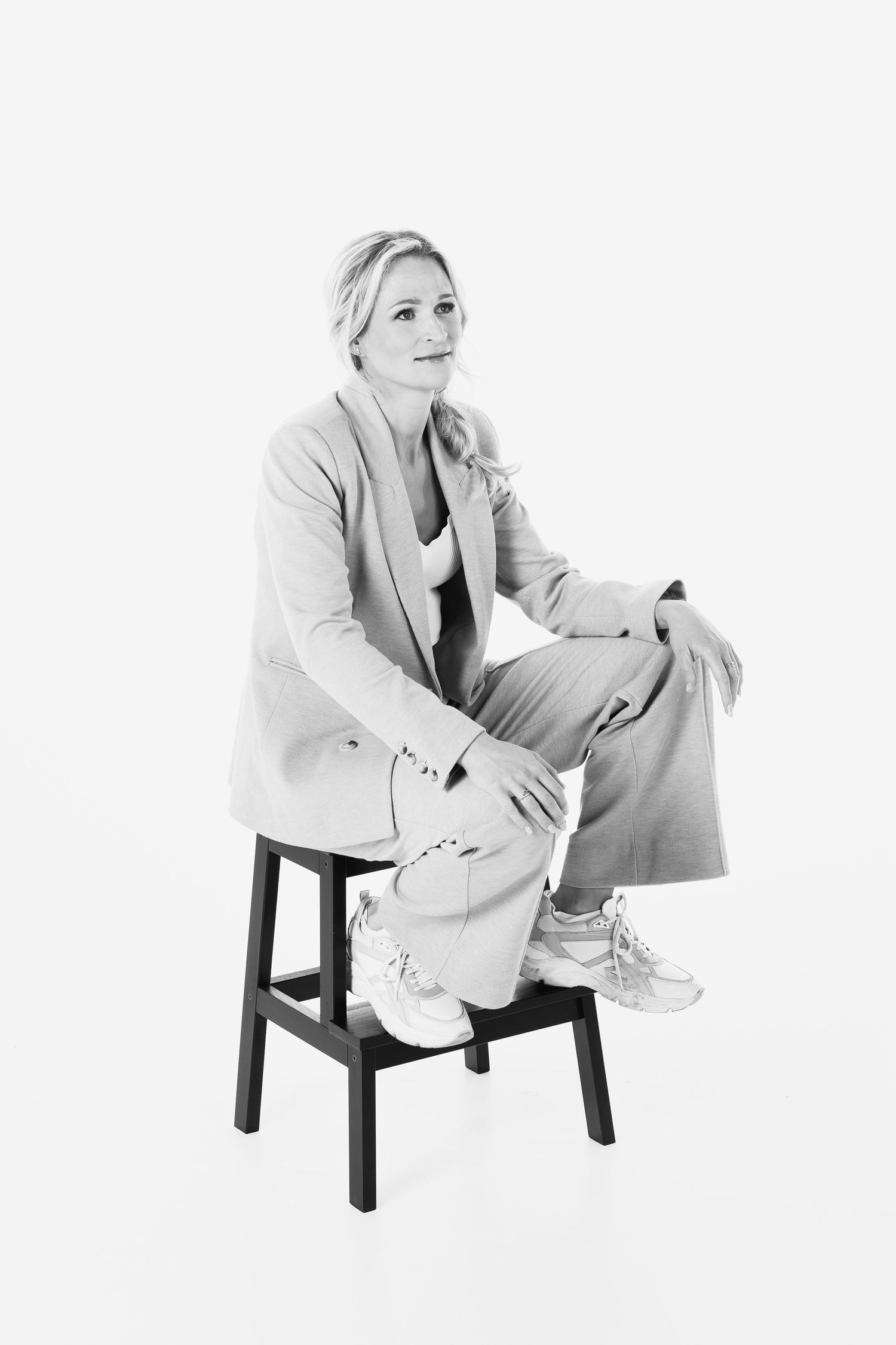Casual business portrait of someone seated on a stool wearing a light colored suit.