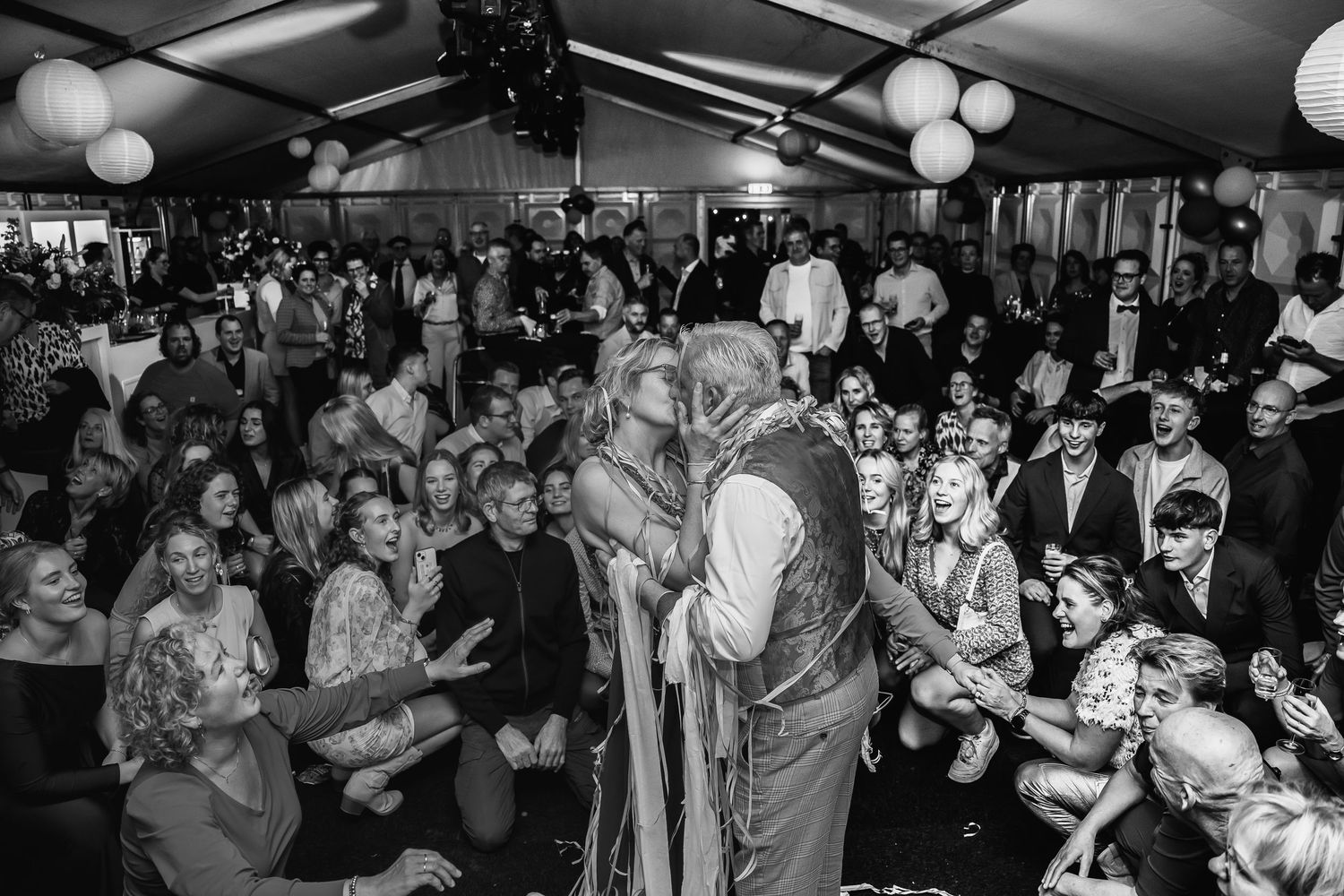 Large crowd gathered under tent for evening celebration with ambient lighting.