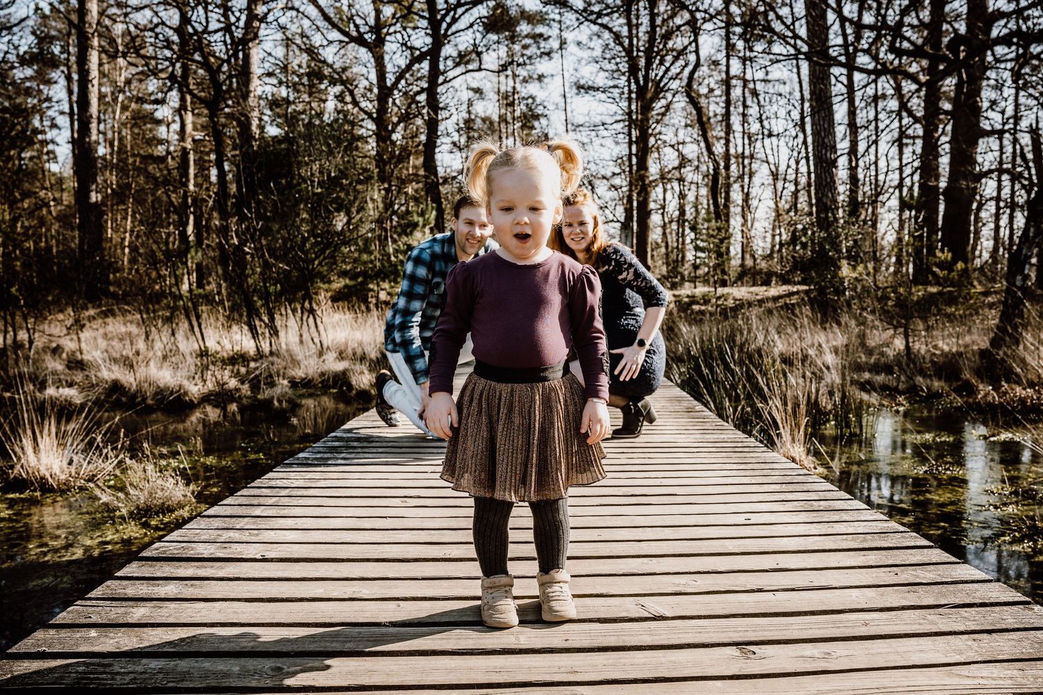 People walking across wooden boardwalk through natural wetland area.