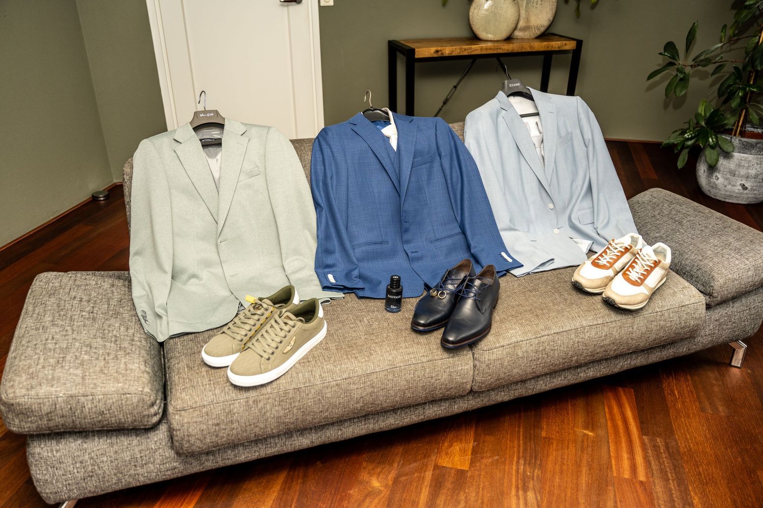 Various formal shoes and clothing items arranged on a gray couch.