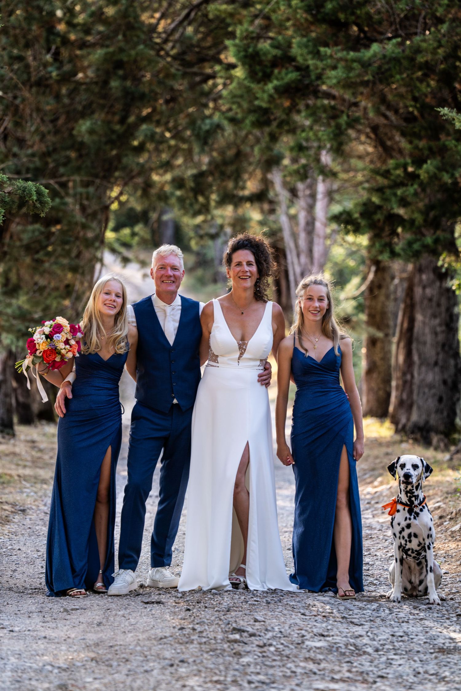 Wedding party walking along a tree-lined path wearing navy blue and white formal attire.