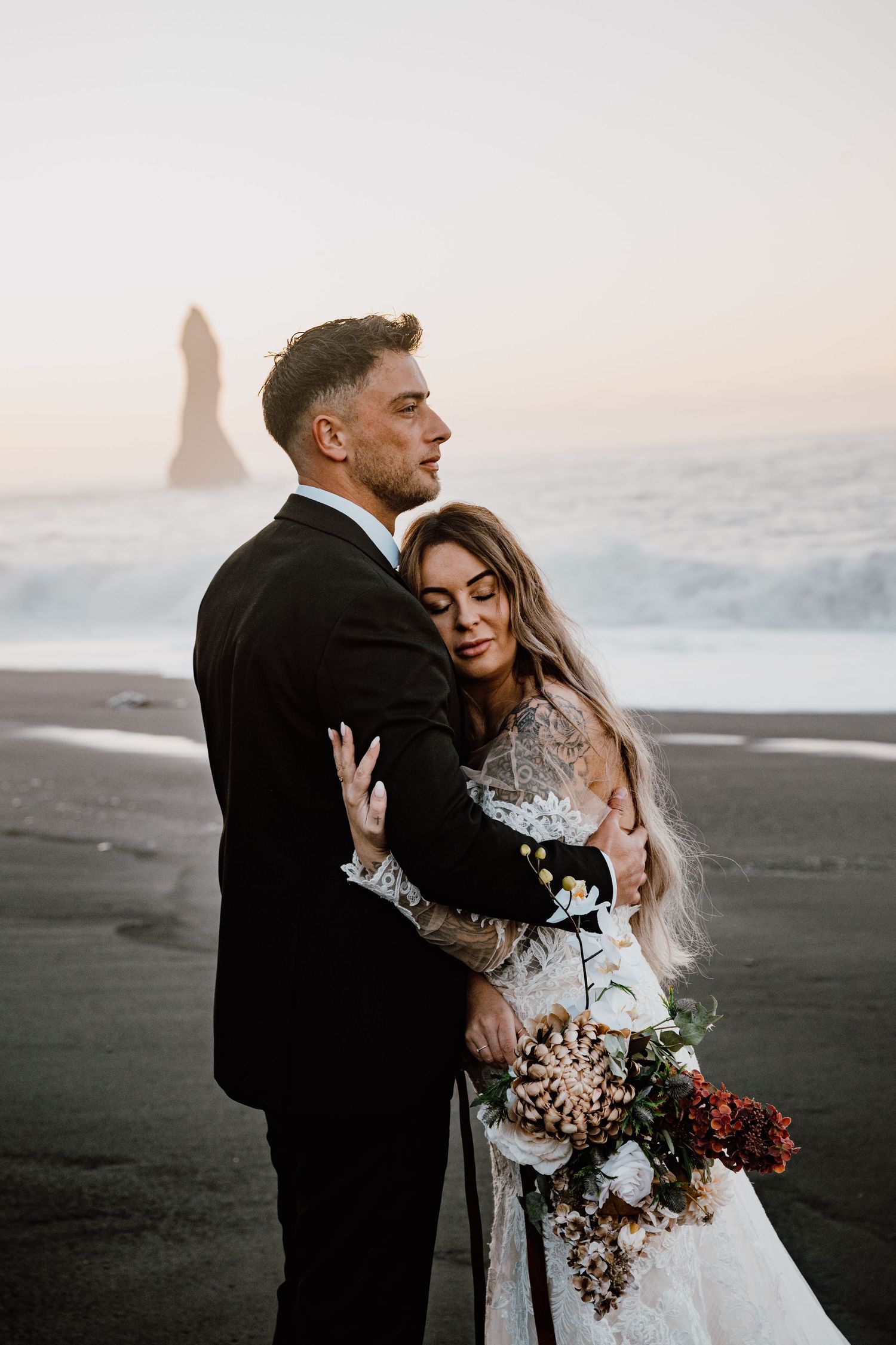 A moody coastal wedding portrait session at sunset with dramatic black sand beach and sea stacks in the background.