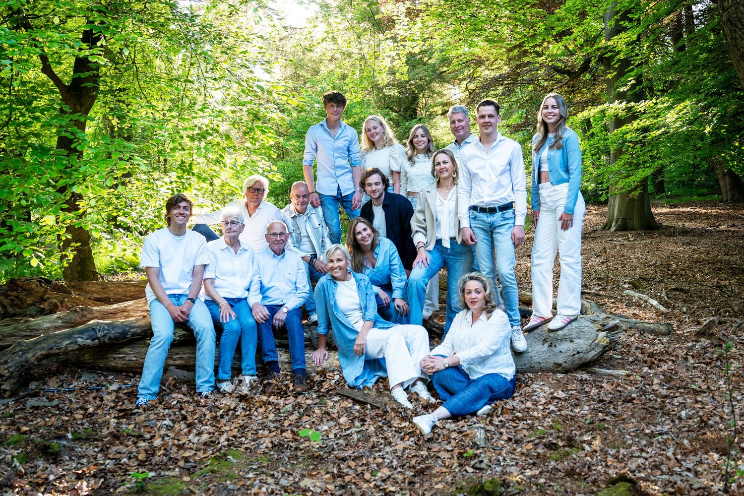 A group wearing white and blue outfits poses together in a wooded outdoor setting during a photo session.