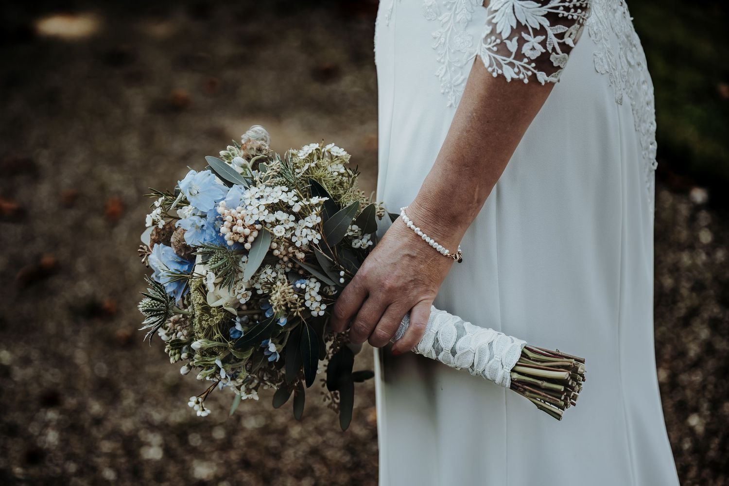 Detail shot of bridal bouquet with white and blue flowers against a white dress.