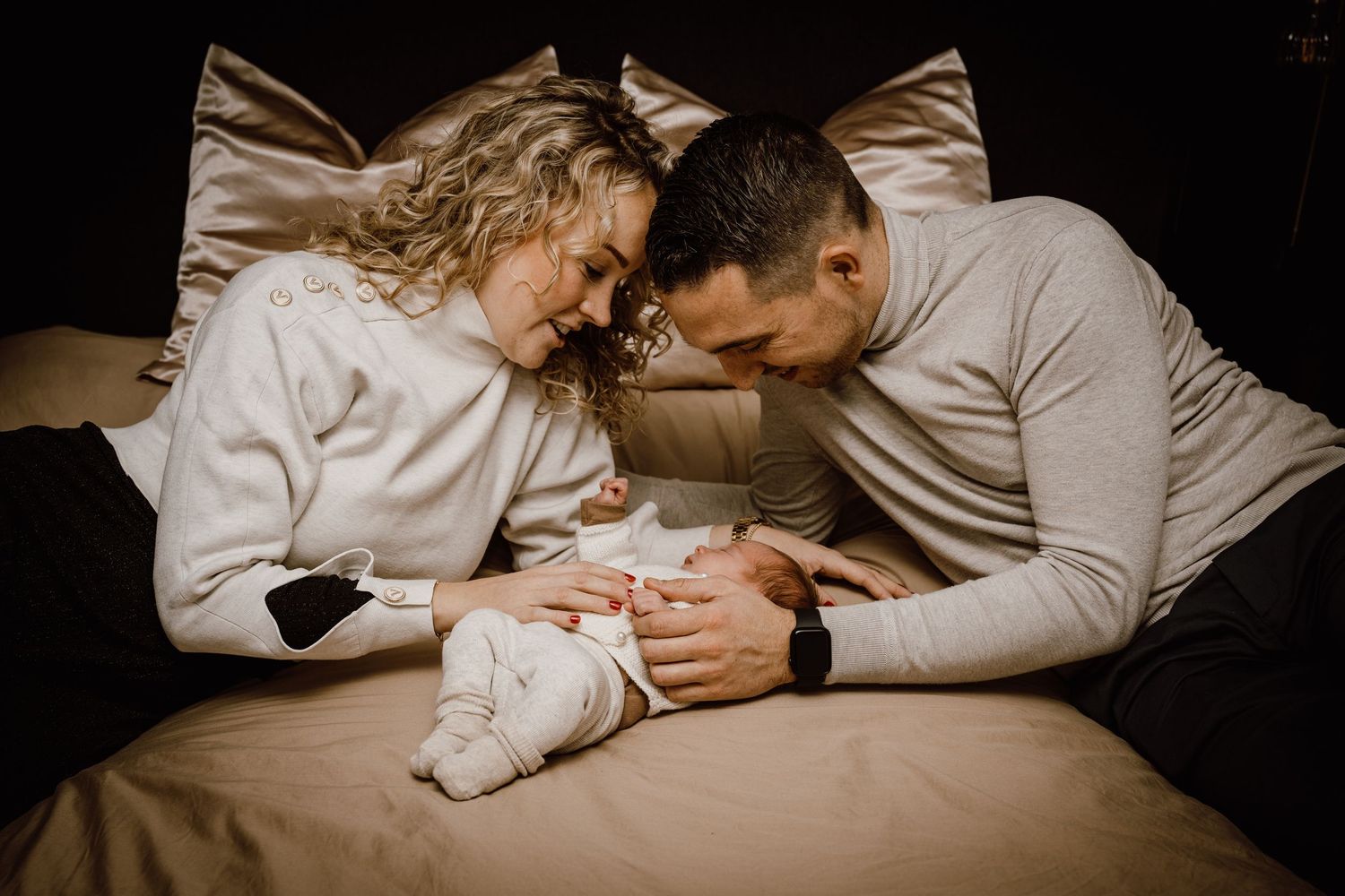 A series of intimate black and white photographs showing a couple cuddling and embracing on dark bedding.