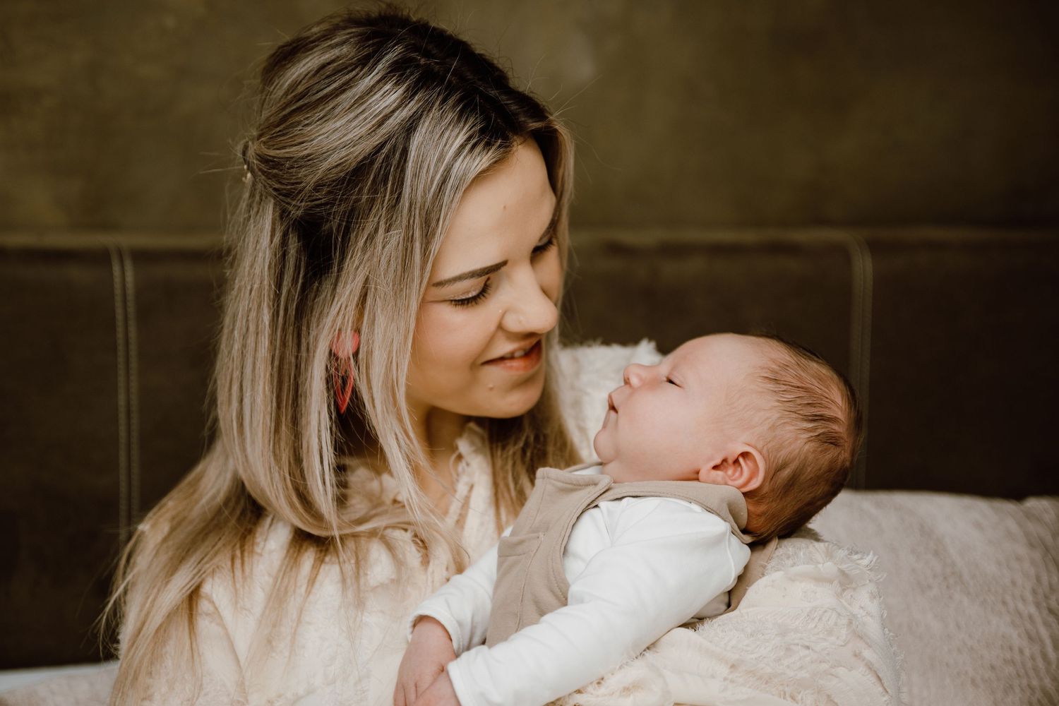 A tender moment between parent and newborn baby in a softly lit room with neutral tones.