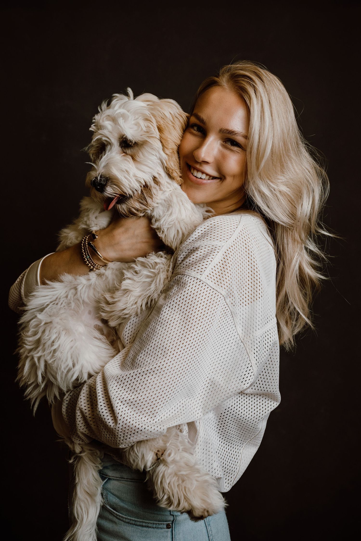 White fluffy dog cuddling with person wearing a white knit sweater against dark background.