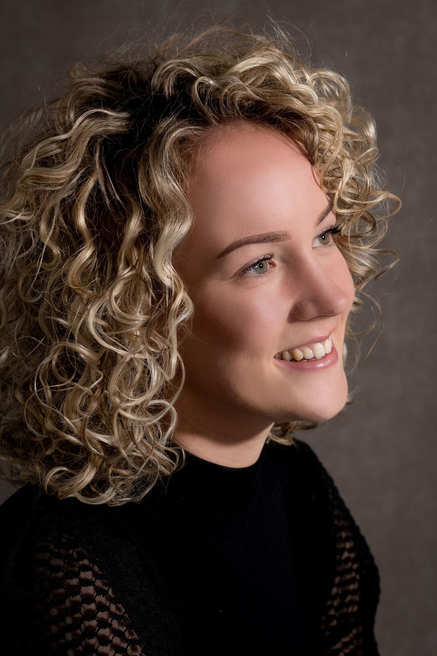 Studio portrait featuring natural curly hair, black top, and warm lighting against dark background.
