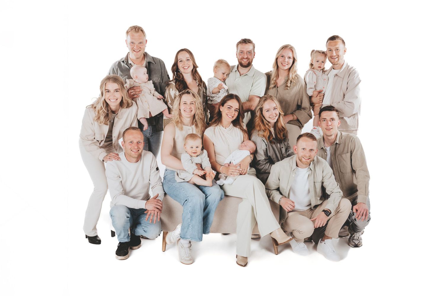 Multiple families dressed in neutral colors pose together on a white studio backdrop.