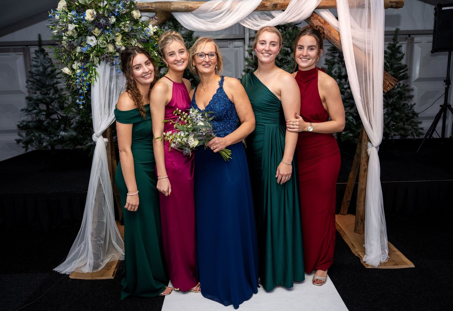Group photo with decorative floral arch and white draping in background.