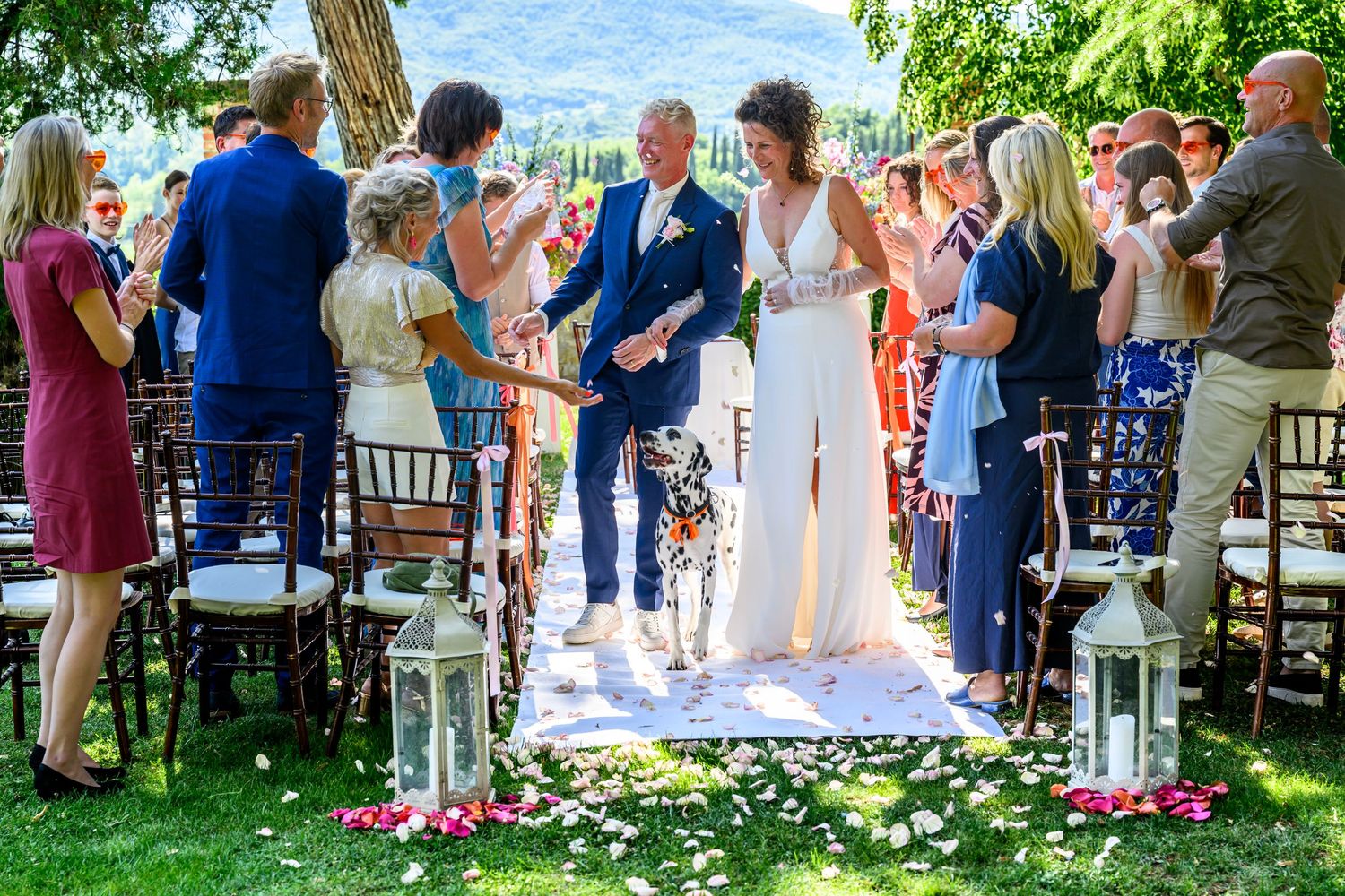 Outdoor garden wedding ceremony with white chairs and flower petals scattered along the aisle.