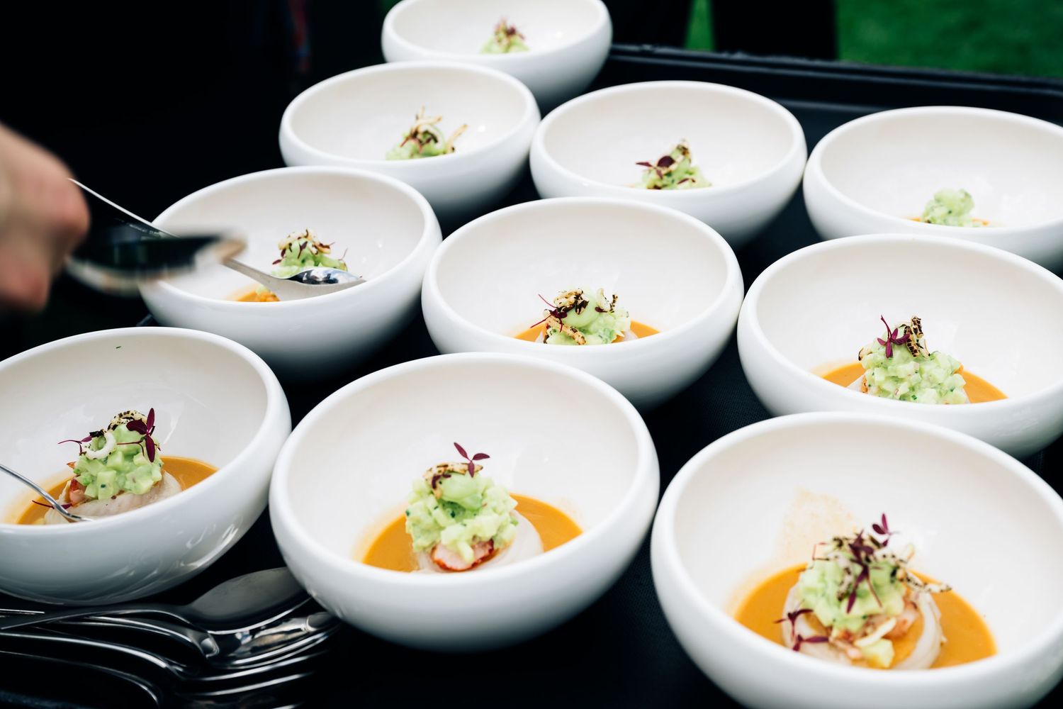 Row of white ceramic bowls with elegantly plated dishes featuring colorful garnishes and sauces.