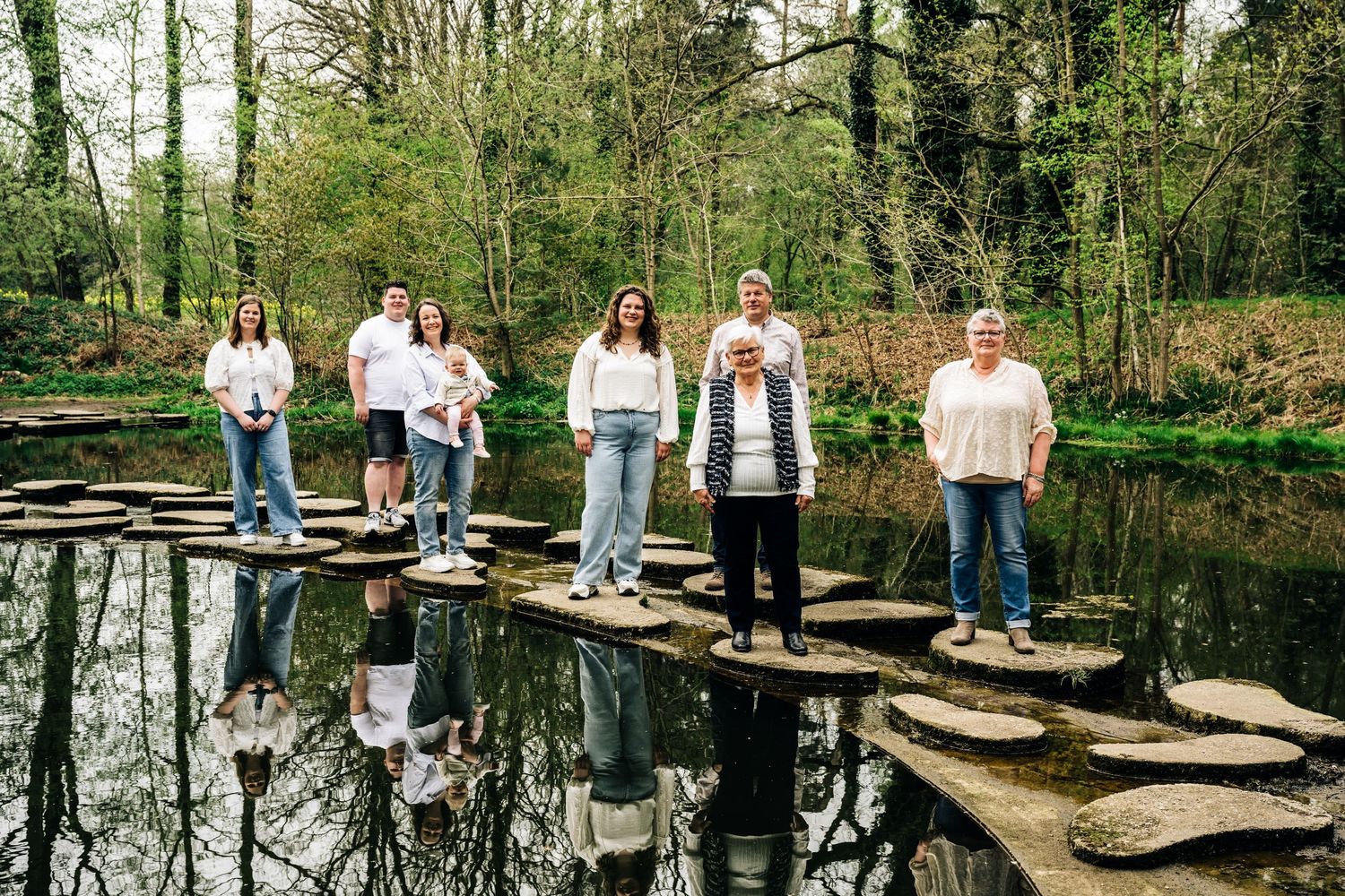 People in coordinated outfits gather on wooden steps near a reflective pond for outdoor photos.