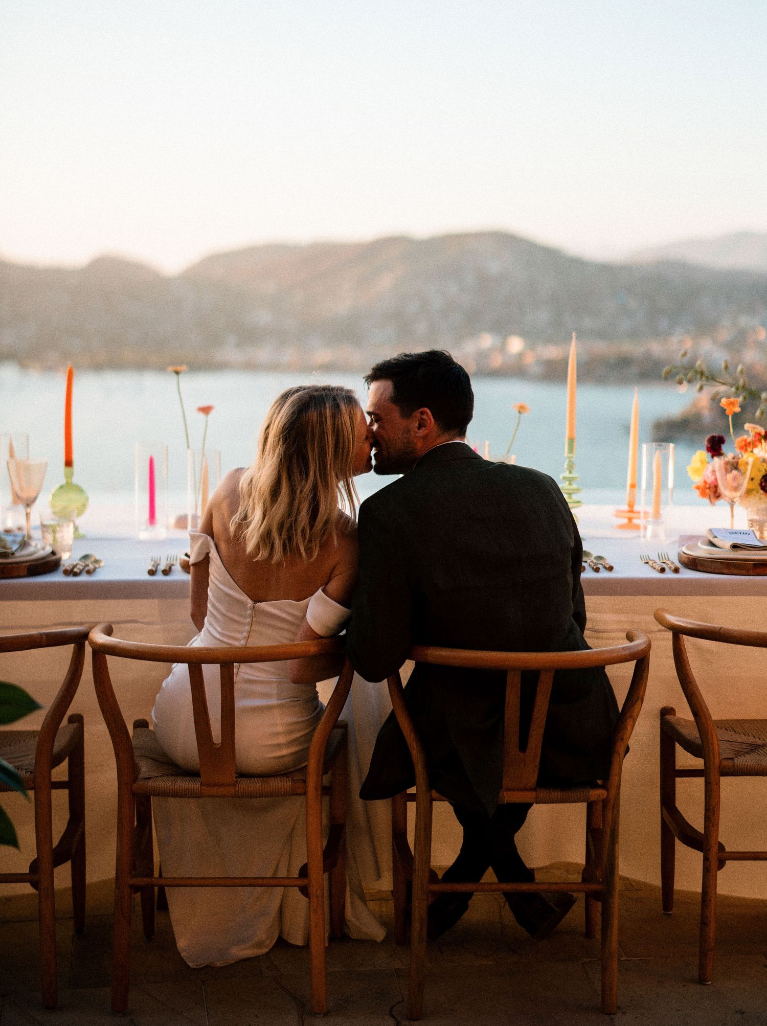 A romantic sunset dinner setting overlooking coastal mountains with a beautifully set table and glowing candles.