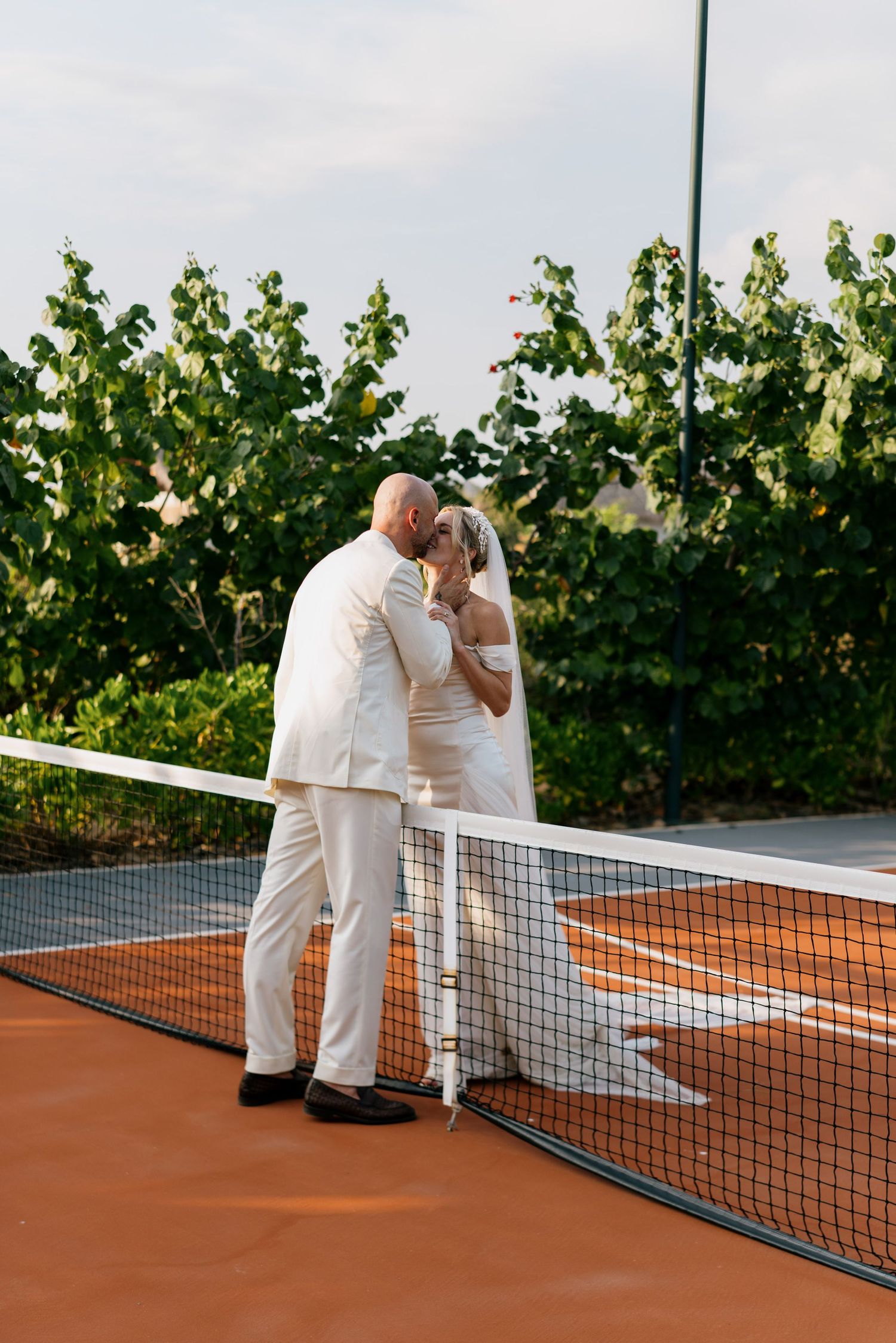 Couple sharing a romantic moment on a tennis court surrounded by lush greenery.