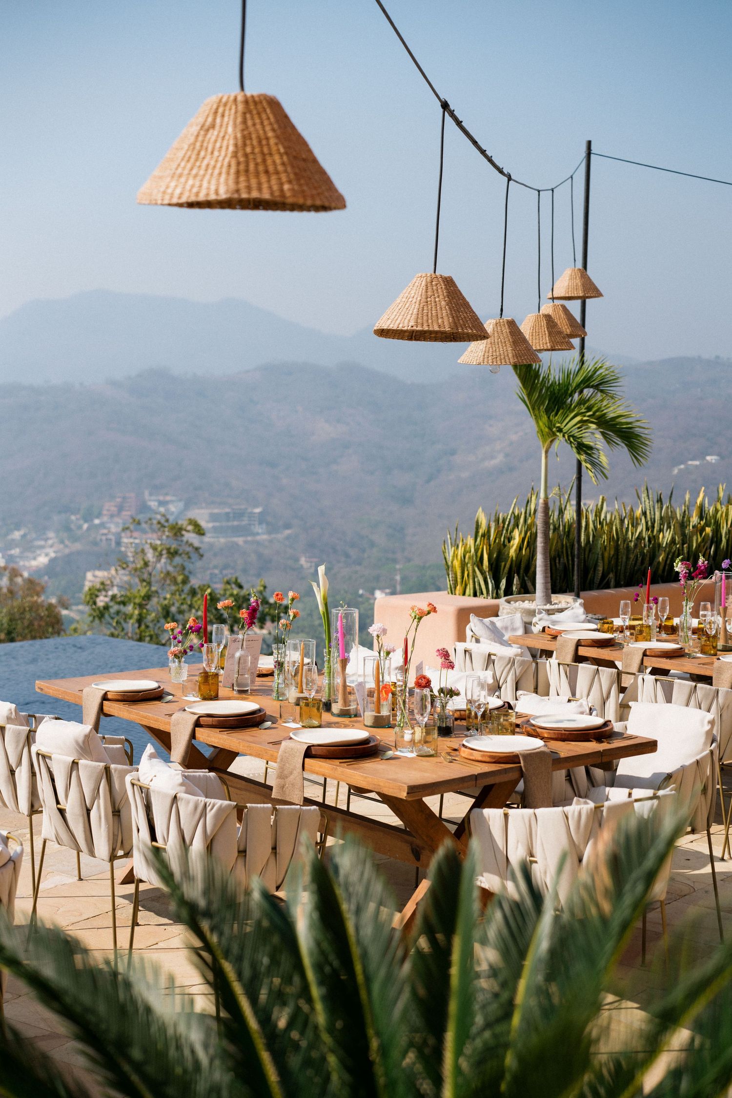 Elegant outdoor dining setup with woven lampshades overlooking a stunning mountain and ocean view.