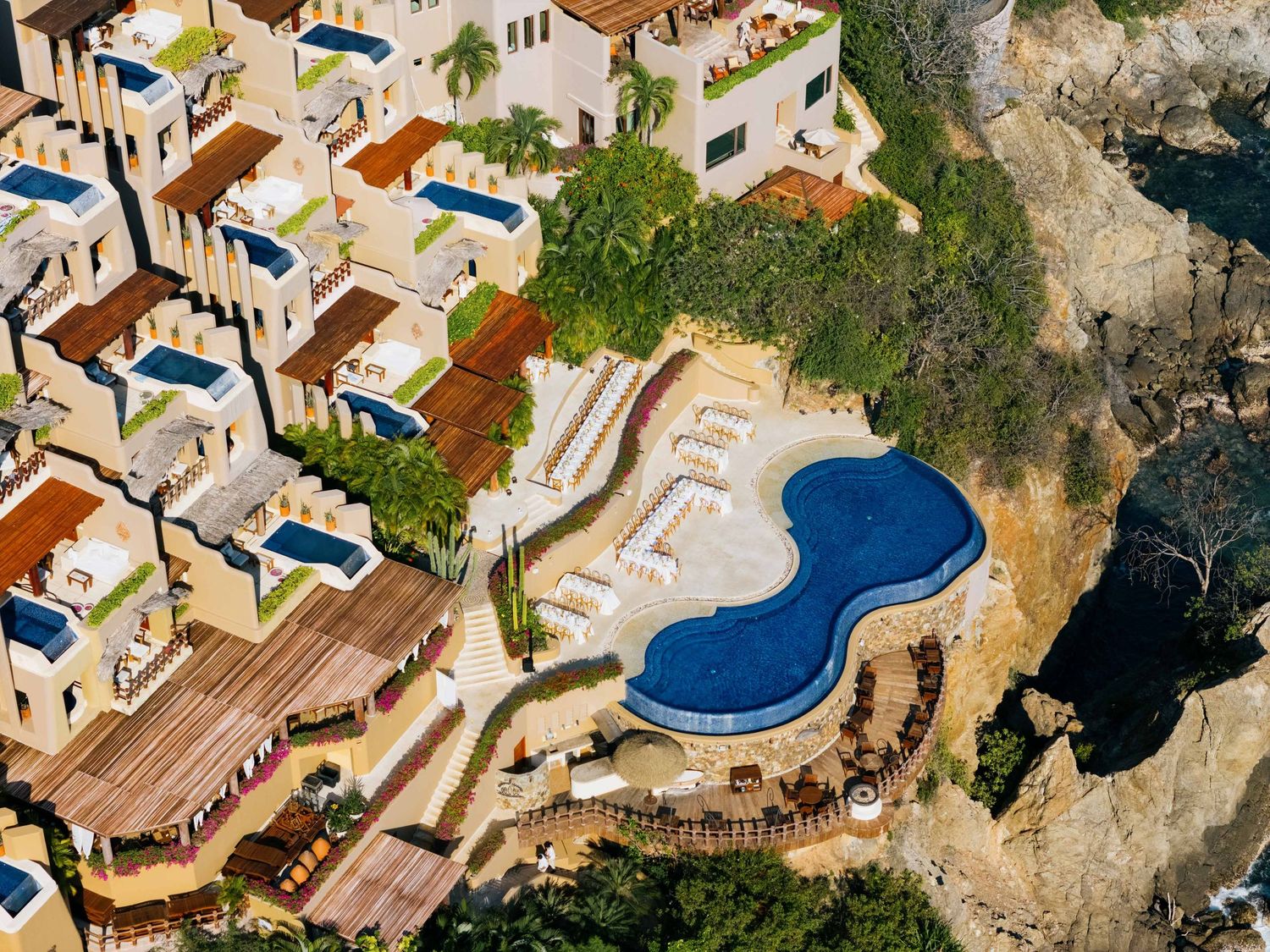 Aerial view of a luxury resort with a curved swimming pool and villas overlooking the ocean.
