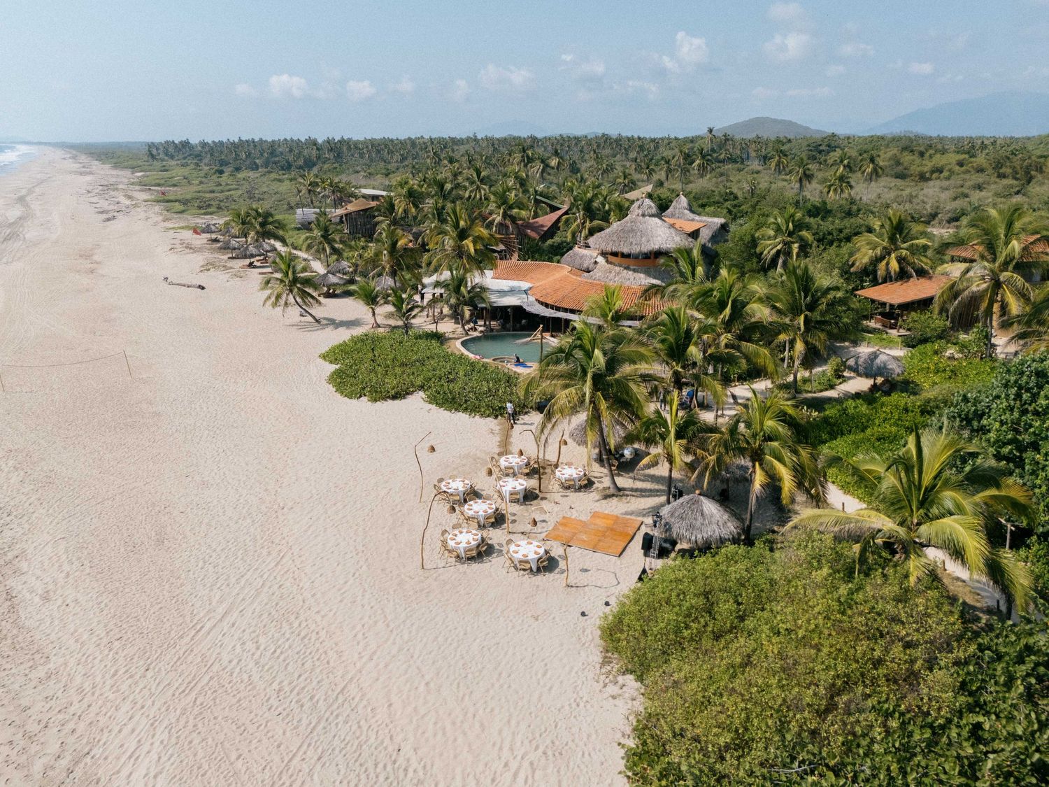 Aerial panorama of a tropical beachfront resort with palm trees and white sand beach.