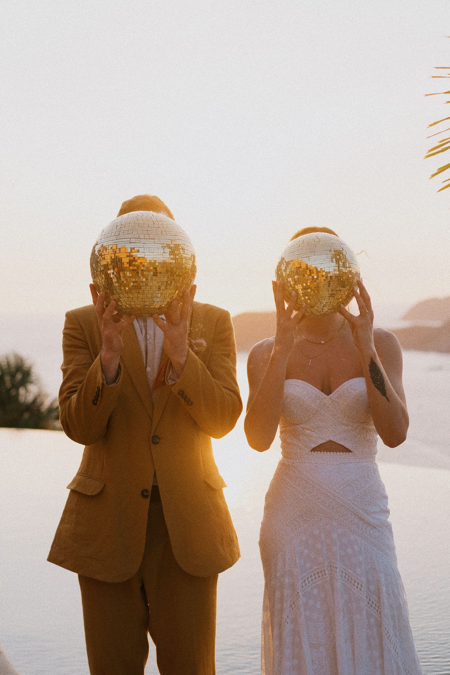 Playful wedding couple holding bread in front of their faces during sunset by the ocean.