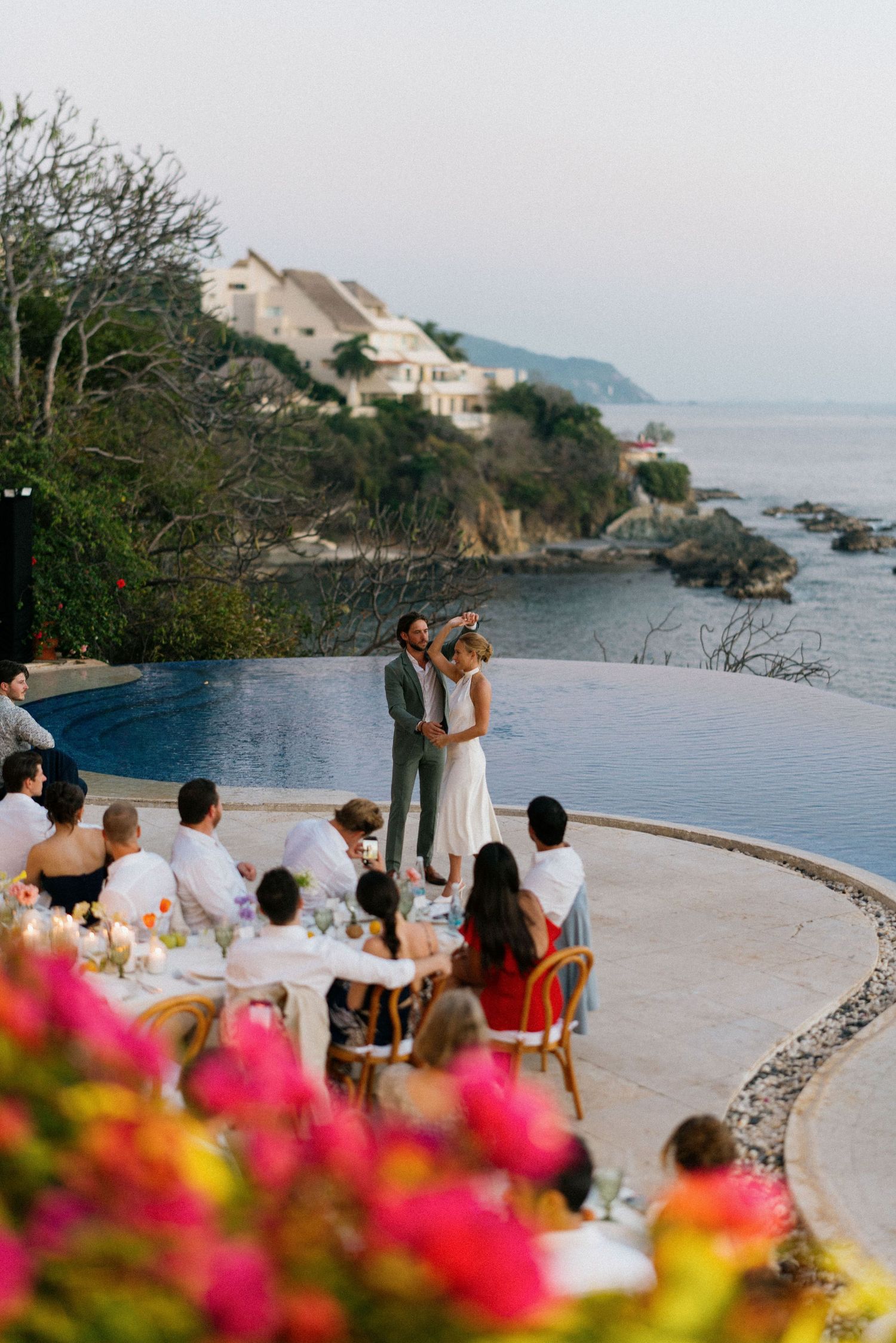 Oceanfront wedding ceremony setup with pink flowers and guests seated facing the water.