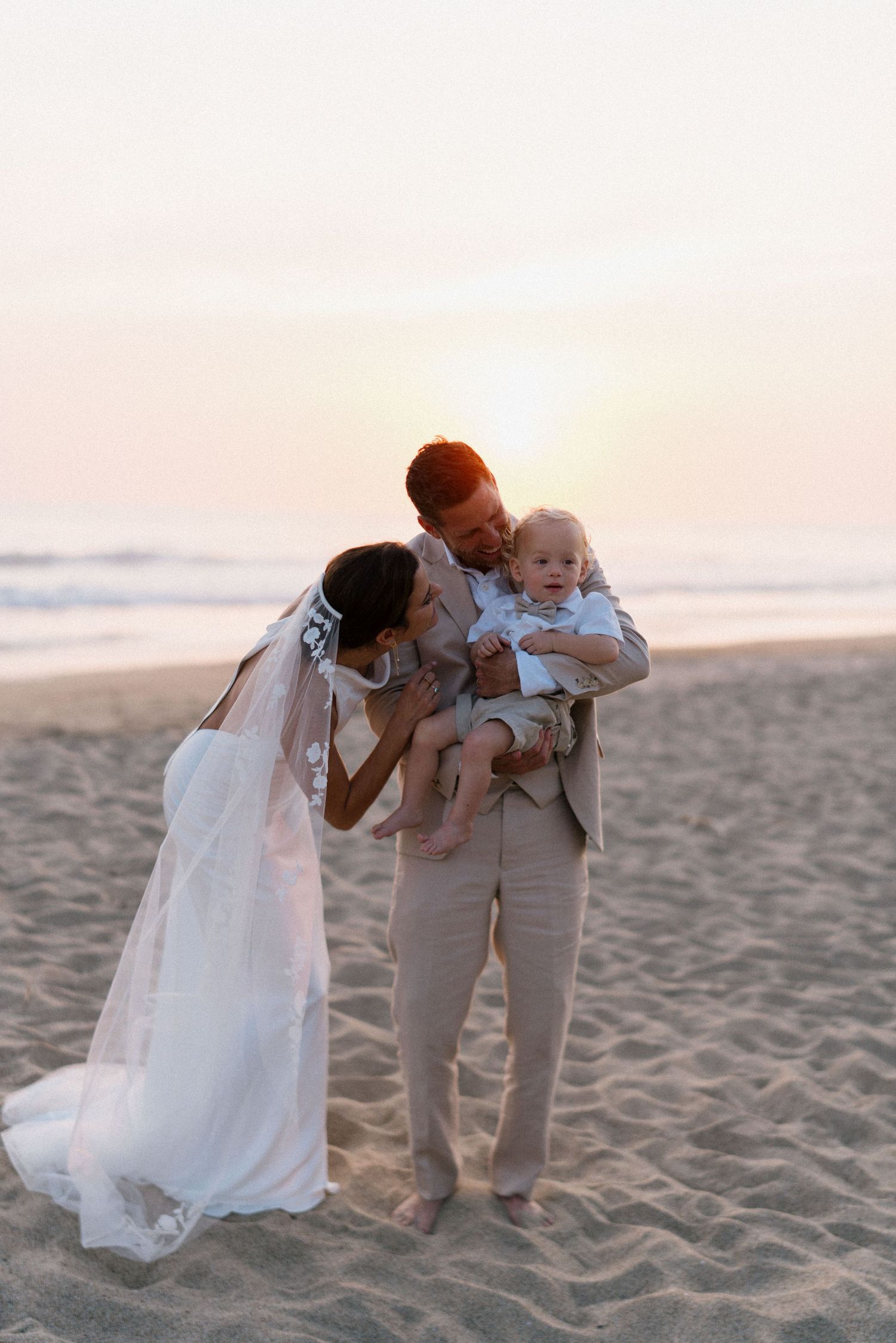 Tender family moment on a beach at sunset with gentle waves in the background.