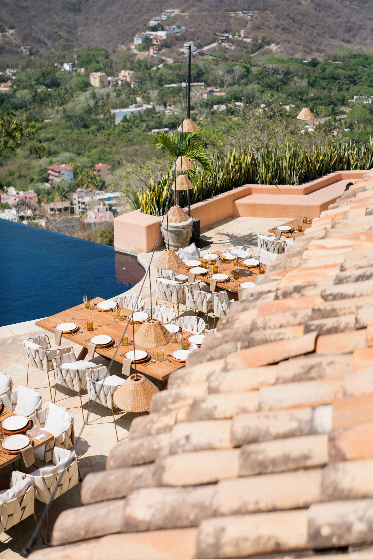 A stunning cliffside terrace with dining tables overlooking a coastal village and blue waters.