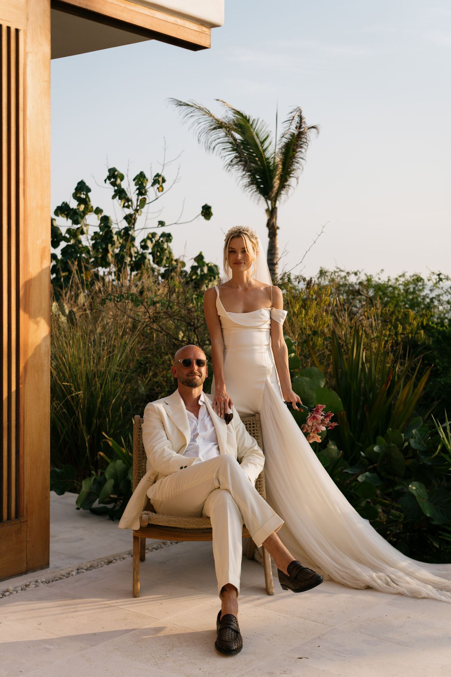 Couple poses in modern outdoor setting with tropical plants and architectural elements.