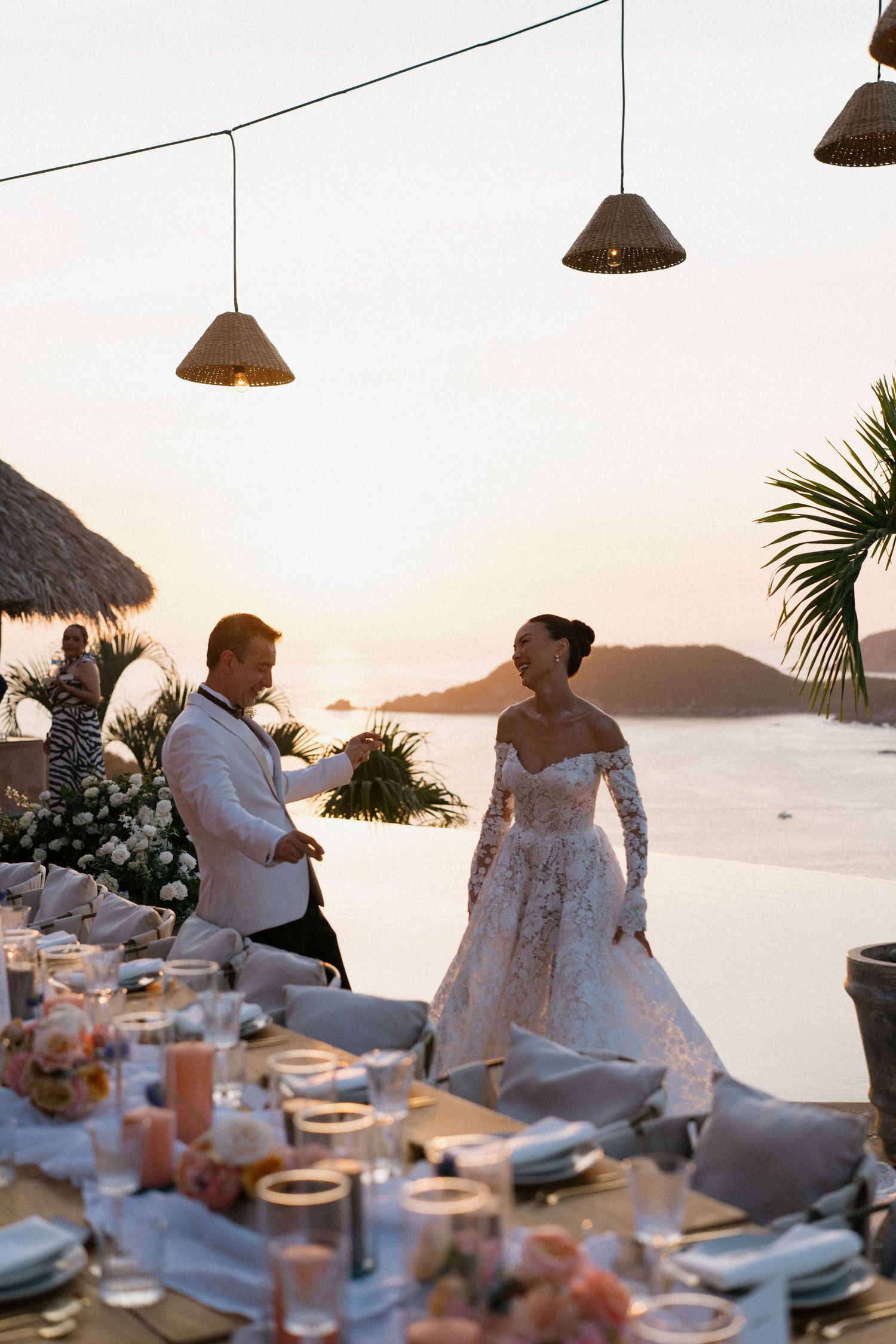 Elegant coastal wedding reception during sunset with string lights and ocean view.