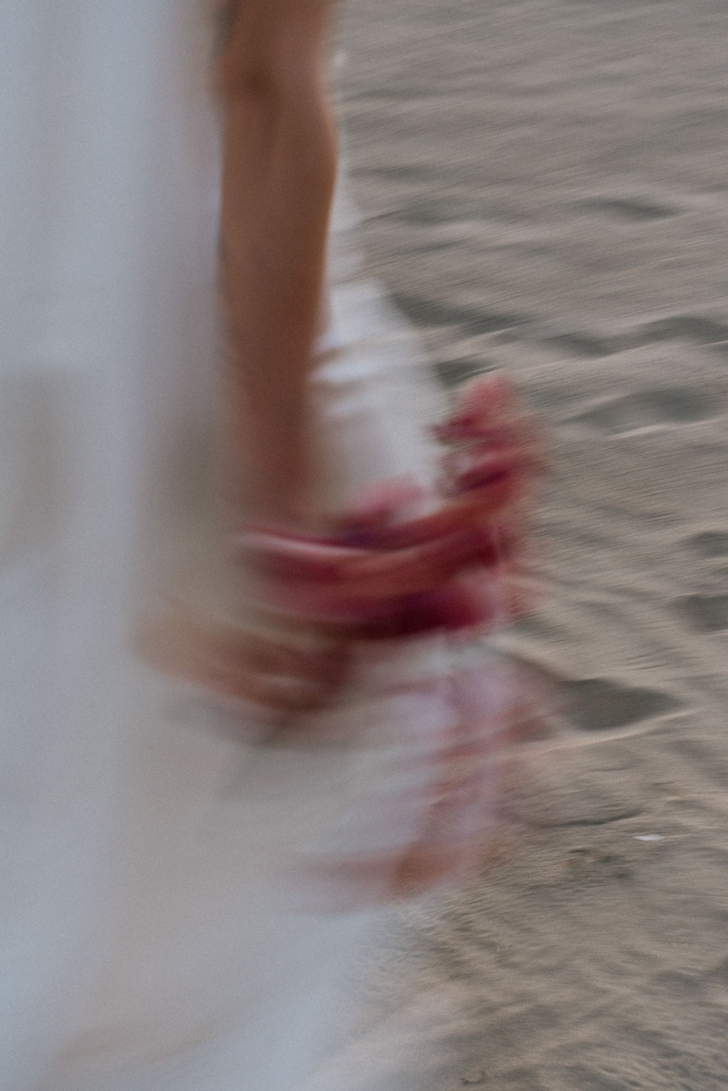 Close-up detail of swishing white fabric against sandy beach.