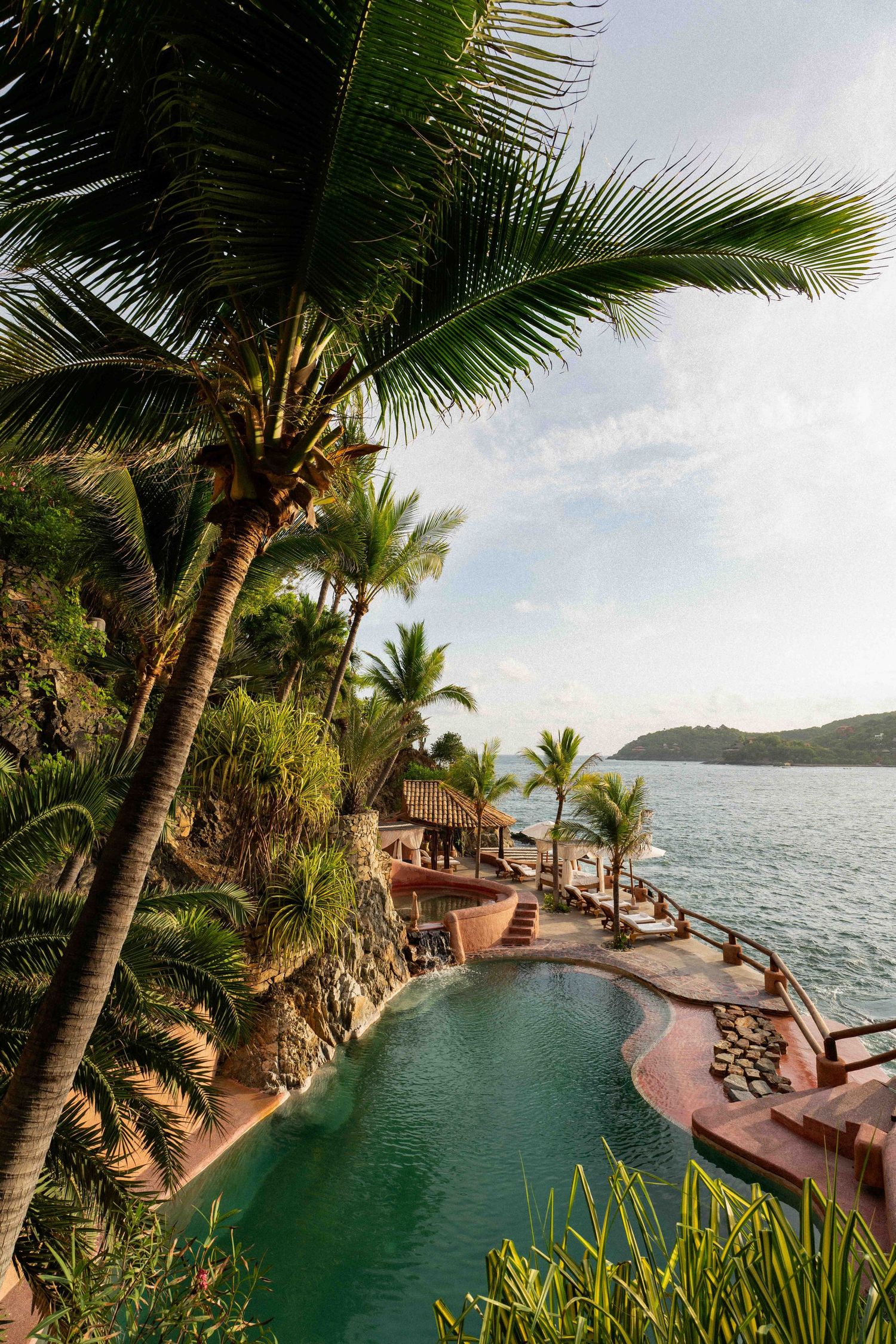 Luxurious infinity pool overlooking a tropical ocean bay with palm trees and lounge chairs at an exclusive resort.