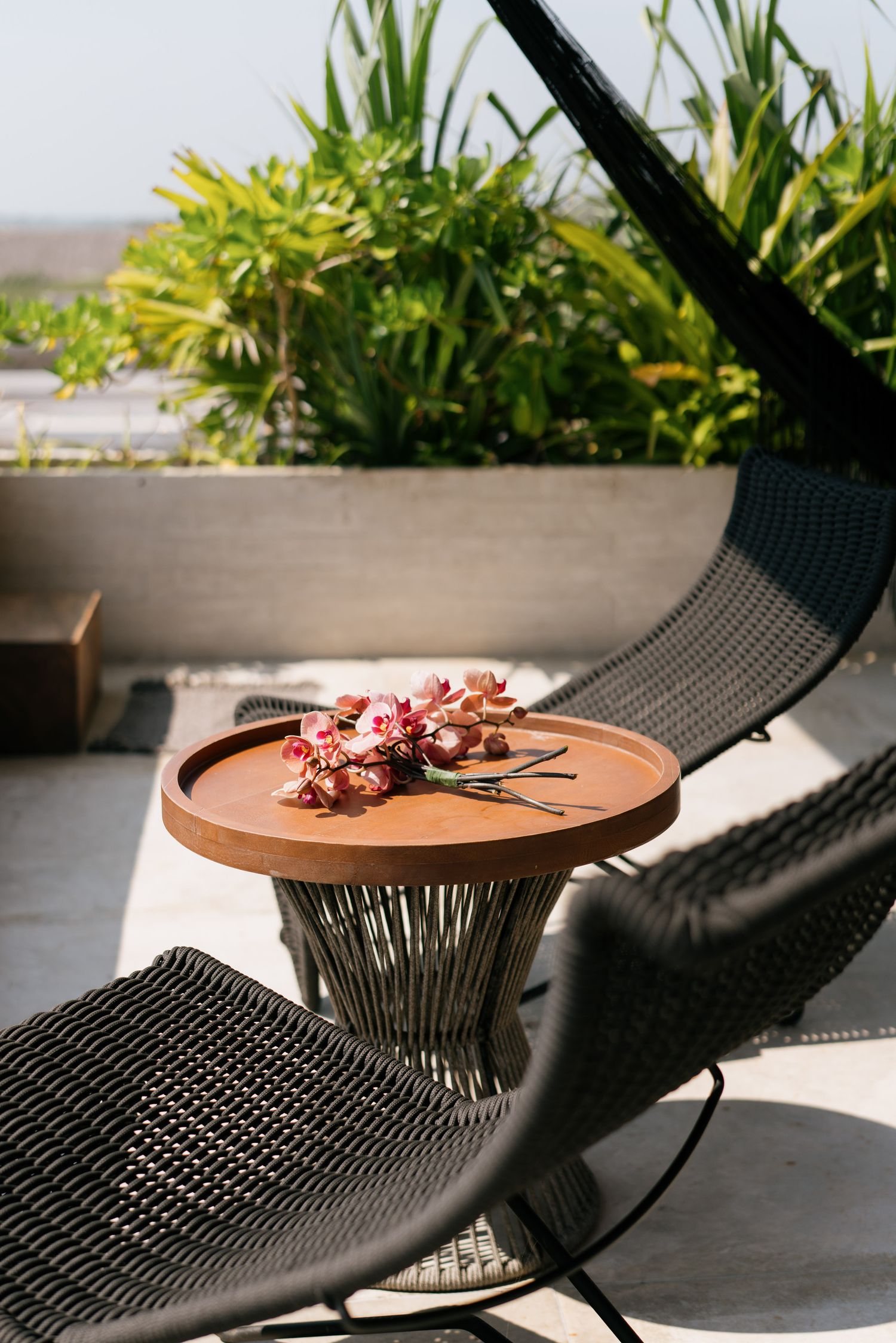 Modern outdoor seating area with black woven chairs and terracotta side table with floral arrangement.