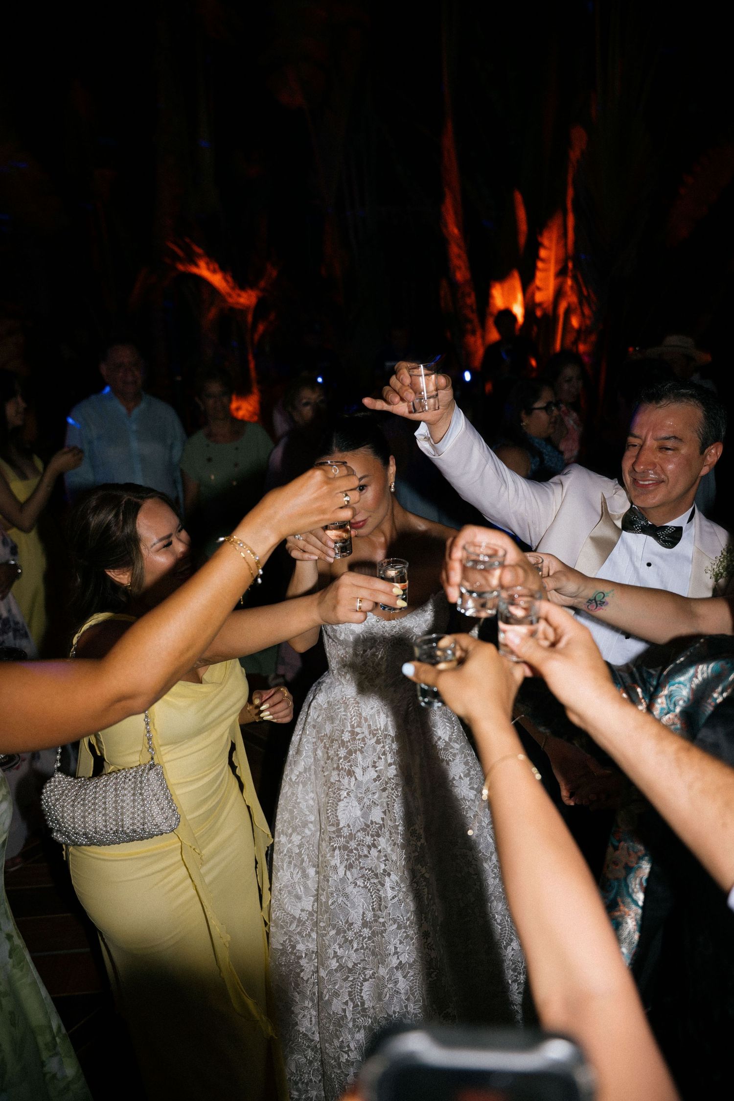 Wedding reception guests raise glasses for a celebratory toast under night sky lighting.
