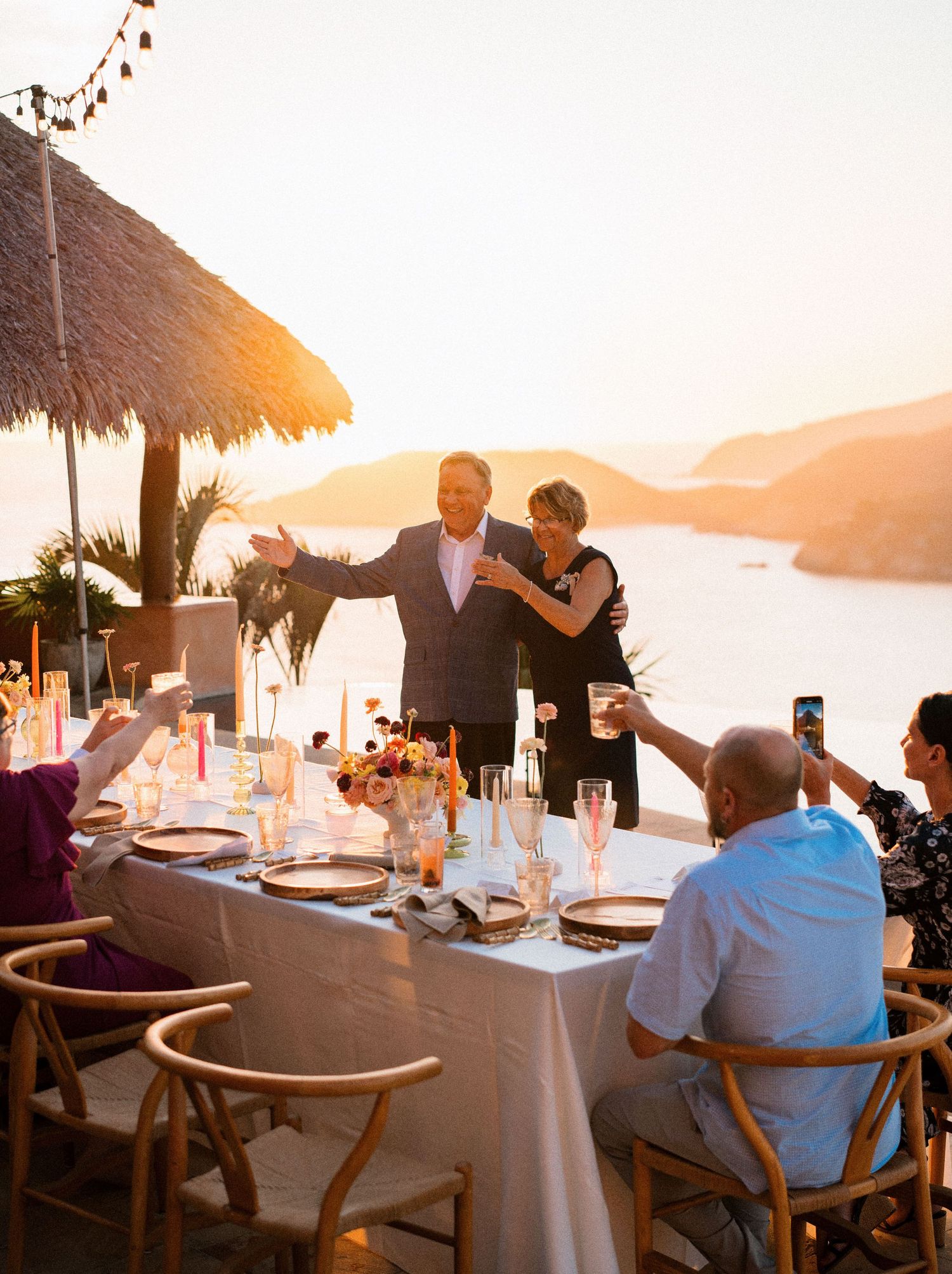 Sunset wedding reception celebration on a coastal terrace with dining tables and guests.