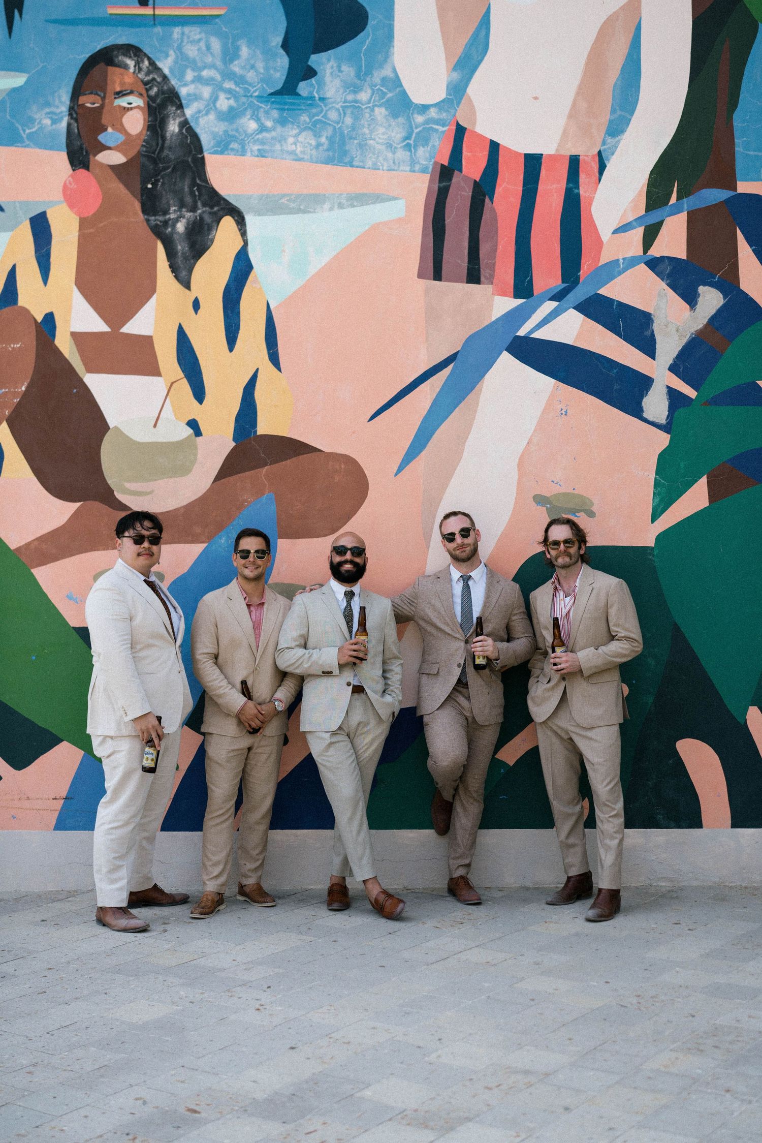 Wedding party posing against a colorful abstract mural wall in light colored suits.