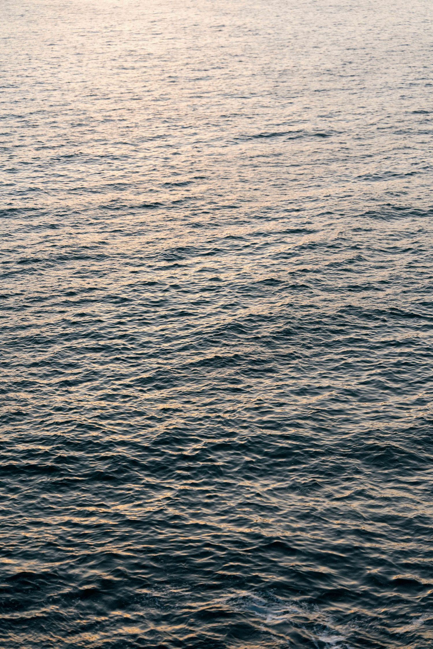 Calm ocean waves ripple across the water's surface during golden hour creating a serene seascape pattern.