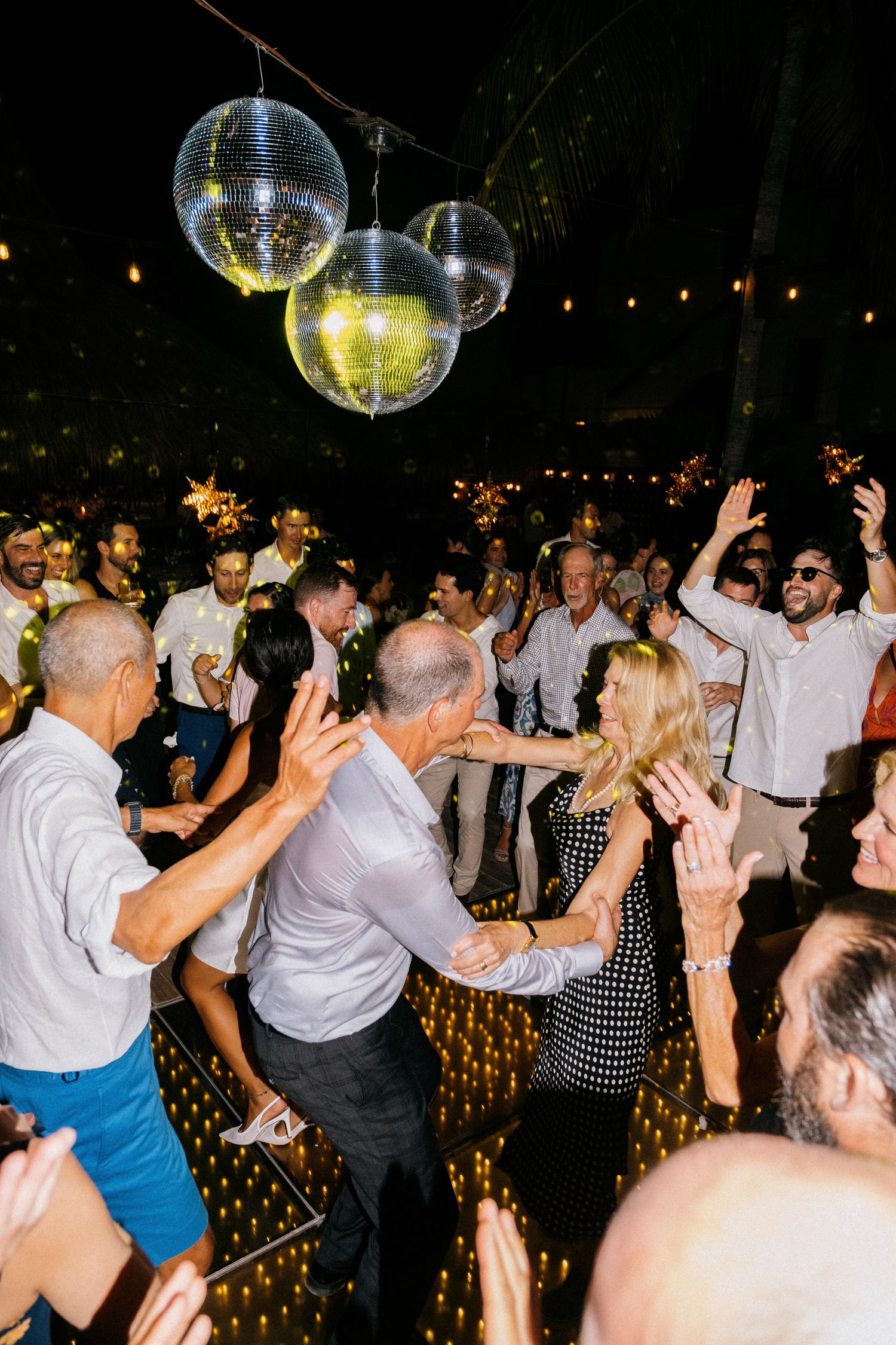 Lively dance floor with disco balls and party guests dancing at a wedding reception.