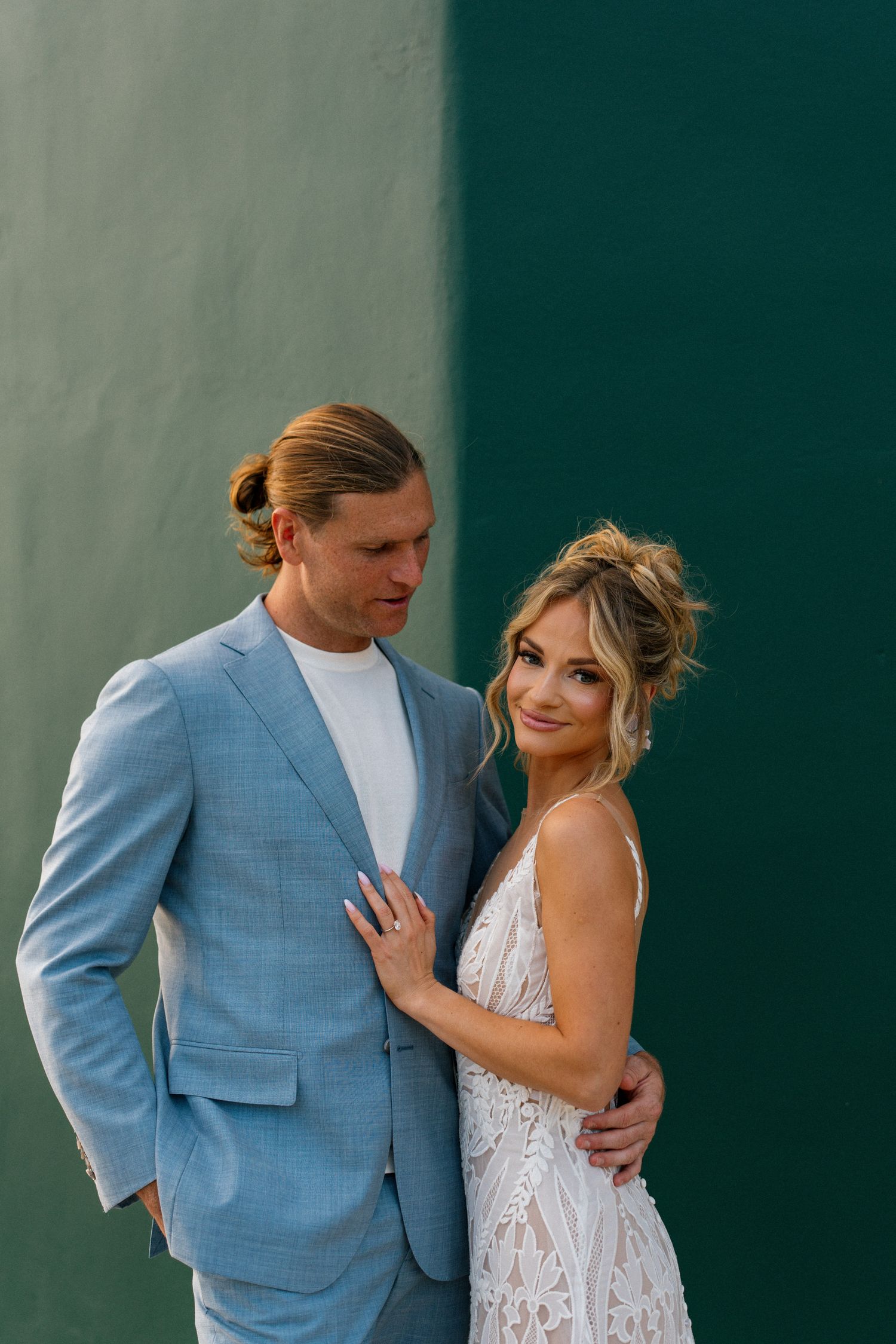 Stylish couple poses against a two-toned green wall in wedding attire.