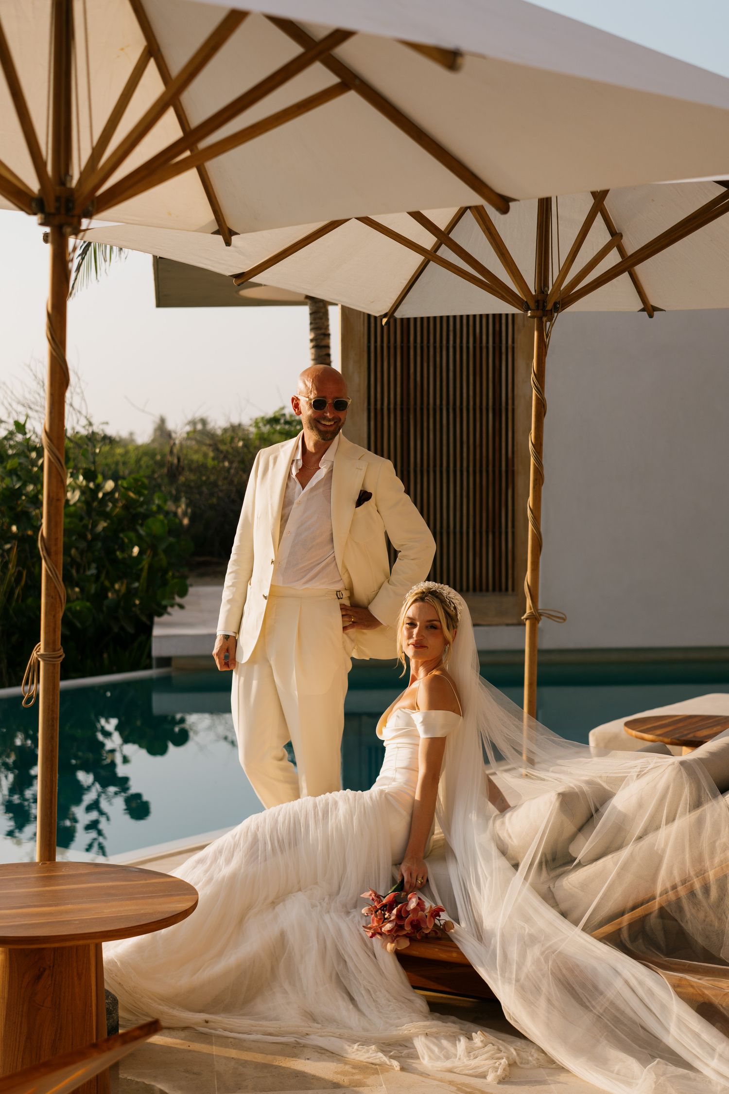Elegant wedding portrait under white umbrellas by a modern poolside setting.
