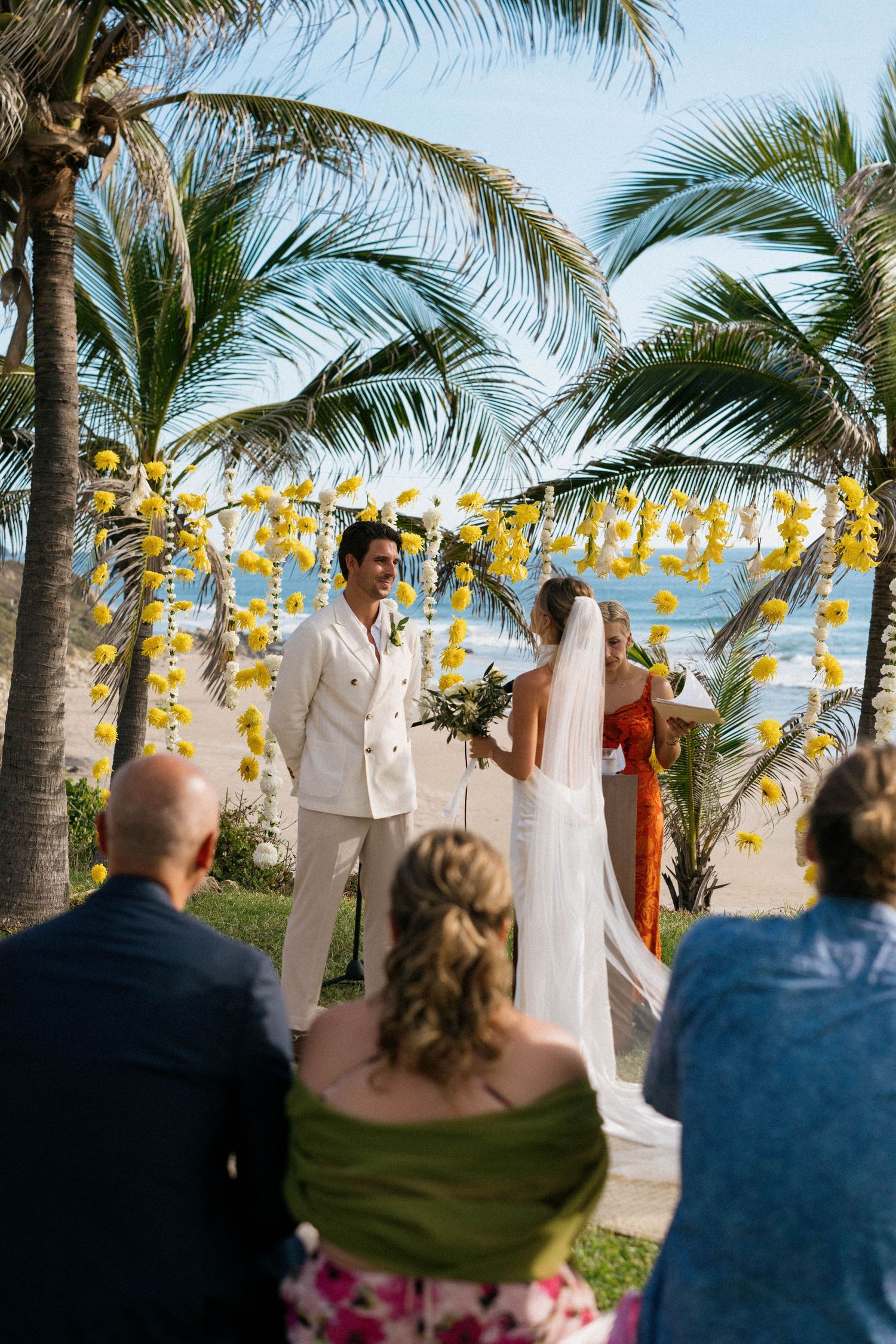 Beach wedding ceremony under palm trees with yellow lantern decorations.