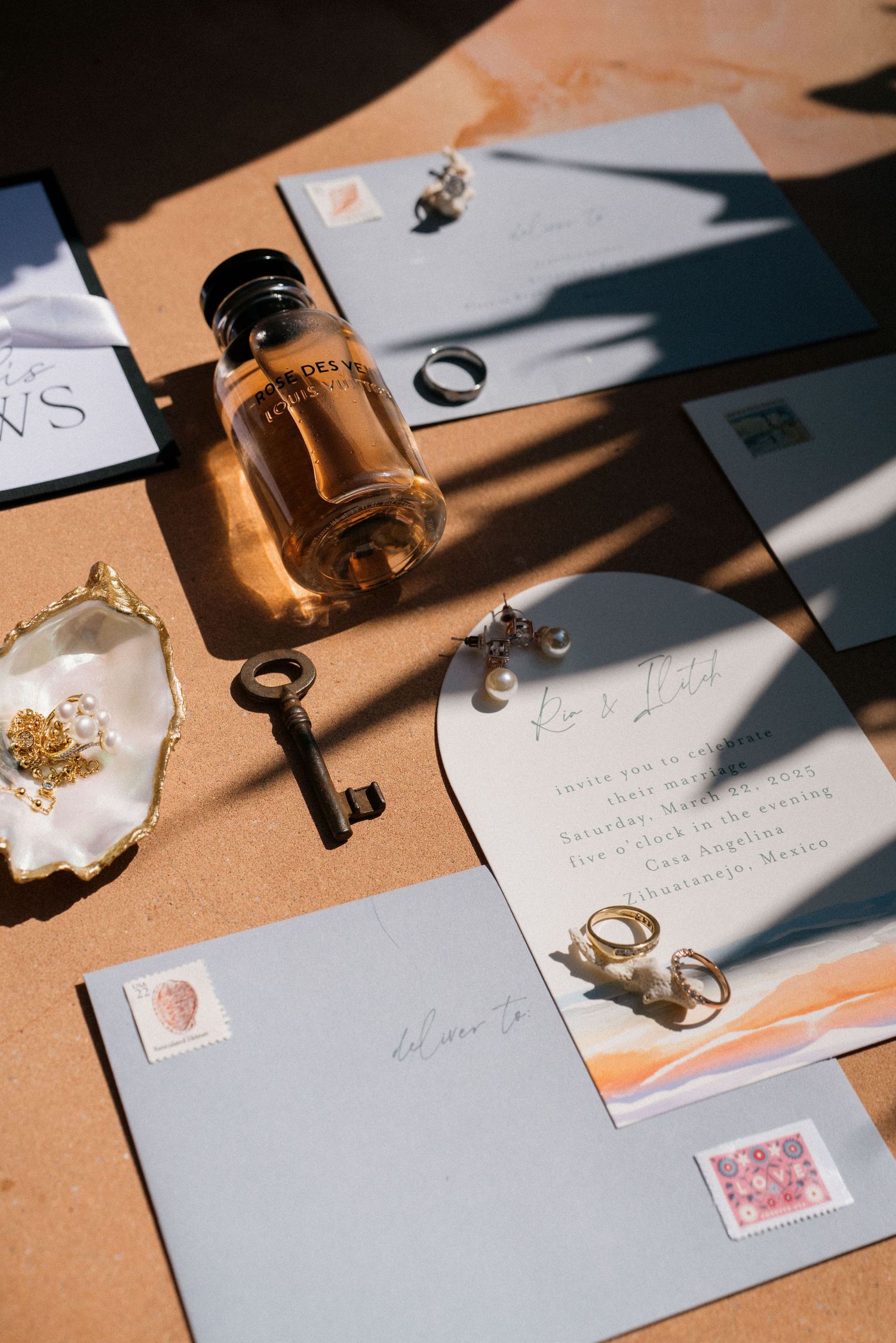 Wedding stationery flatlay with vintage key, rings, and invitation in warm sunlight.