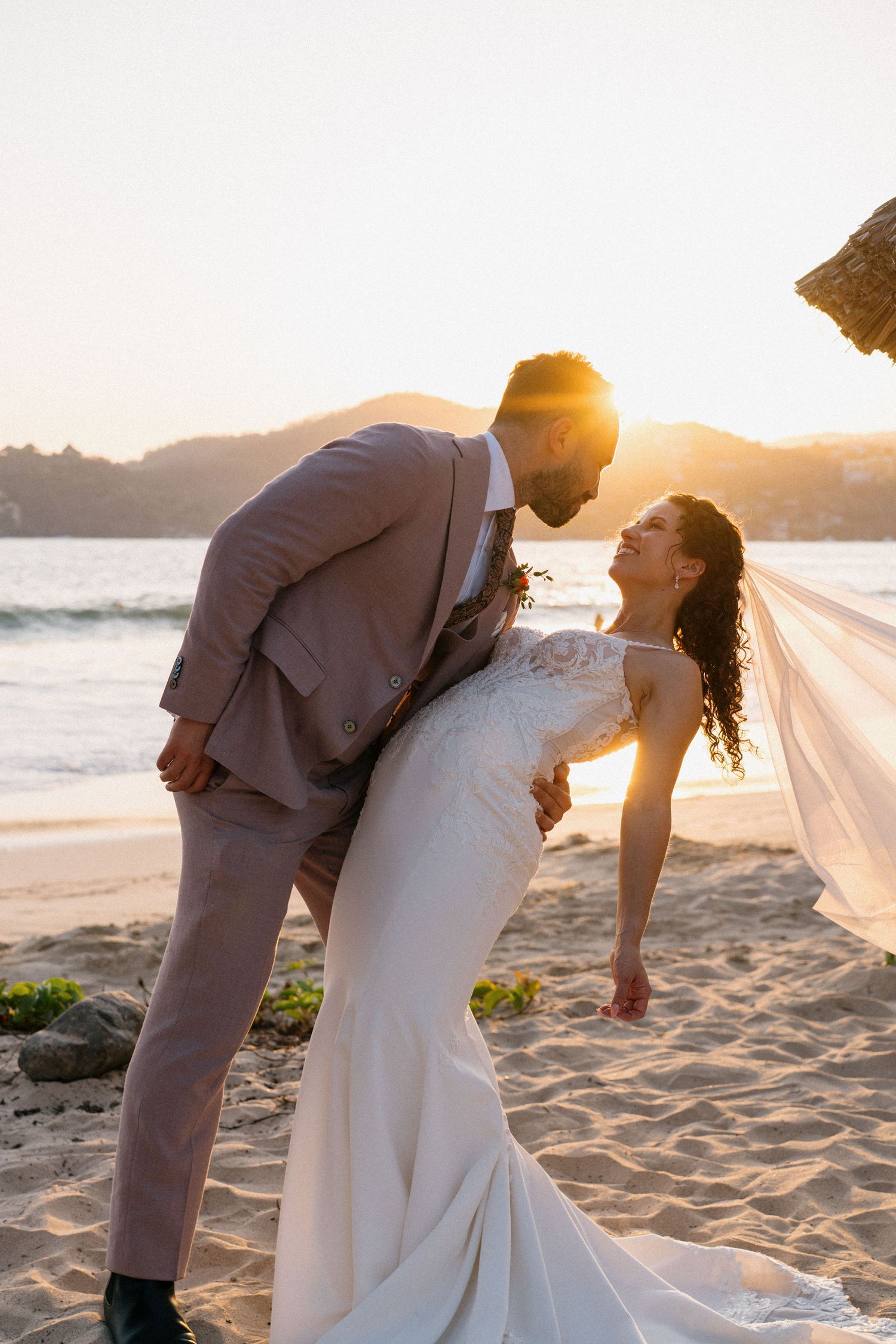 Romantic sunset beach wedding portrait with flowing veil and golden light.
