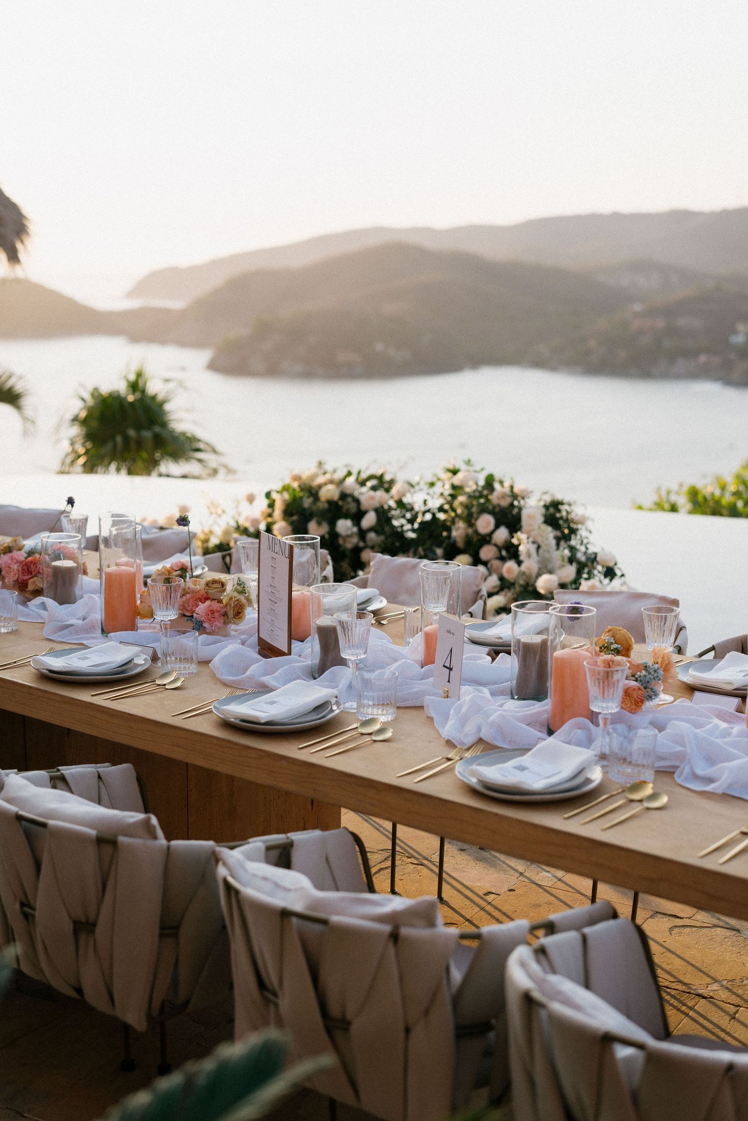 Elegant table settings with ocean view at destination wedding reception in white and neutral tones.